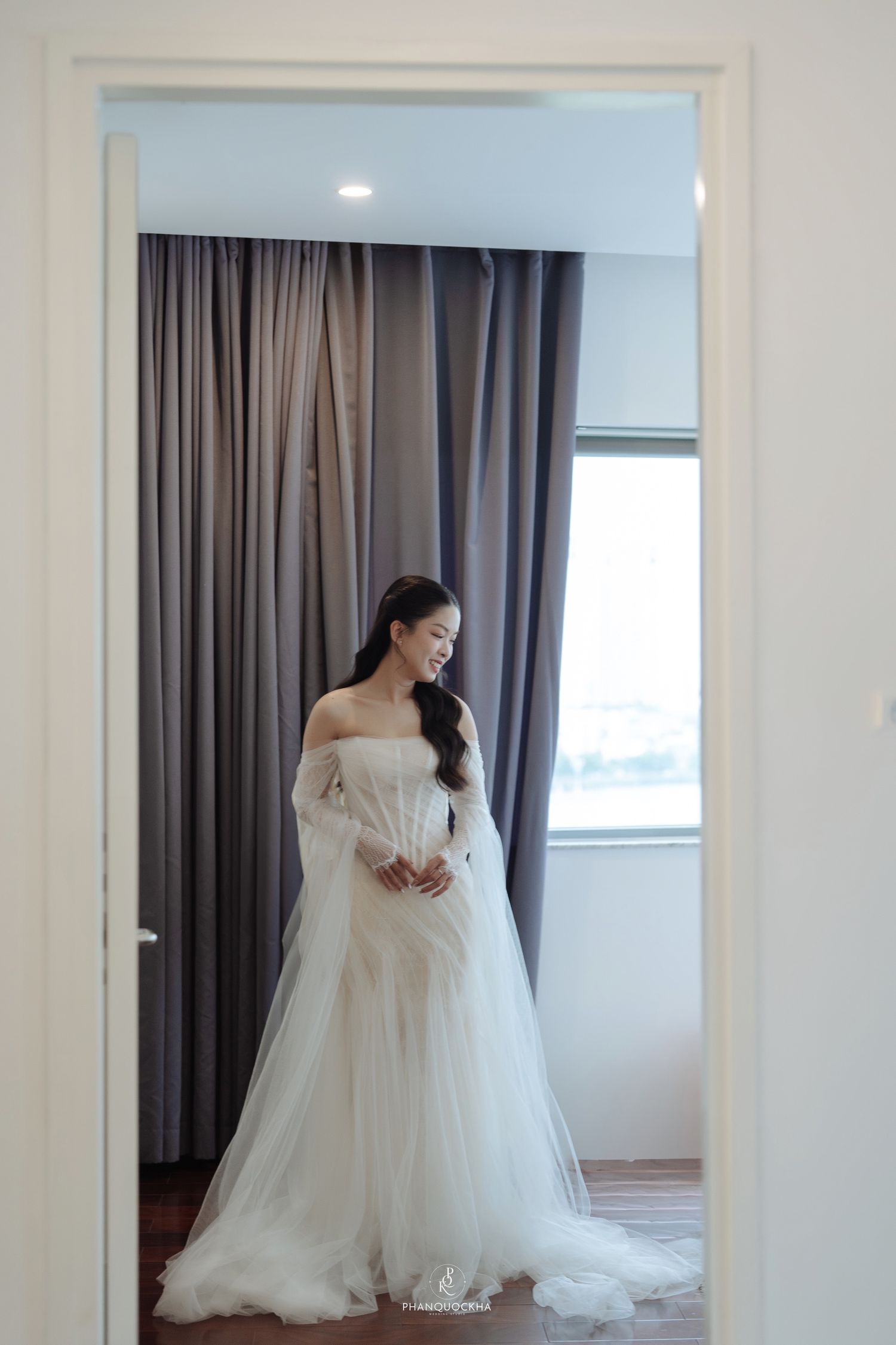 Elegant Asian bride in off-shoulder white tulle wedding gown standing in a doorway.