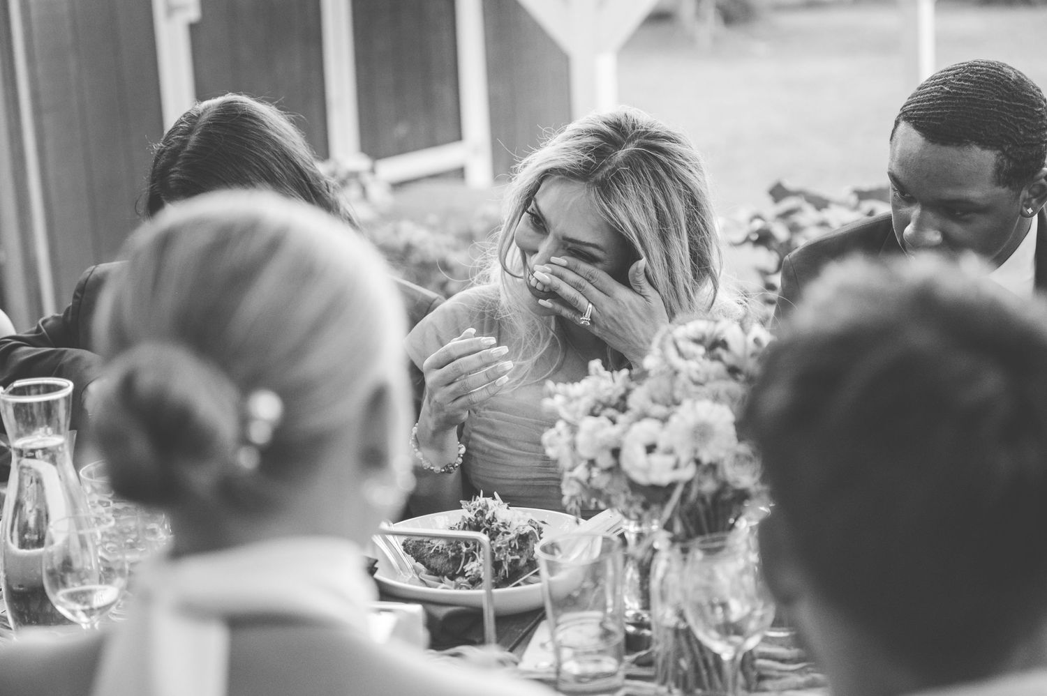 A black and white photo of multiple people sitting around a table, engaged in a lively conversation during a meal.