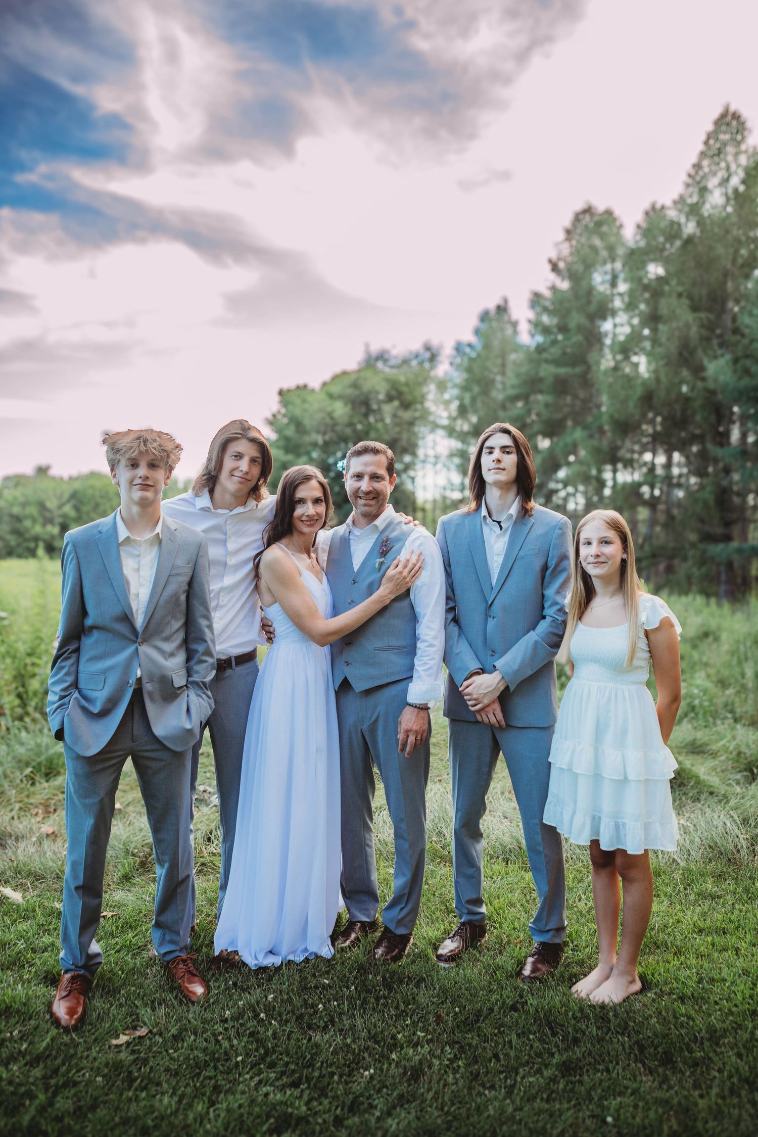 Wedding party in light blue dresses and gray suits poses together on a grassy hillside.