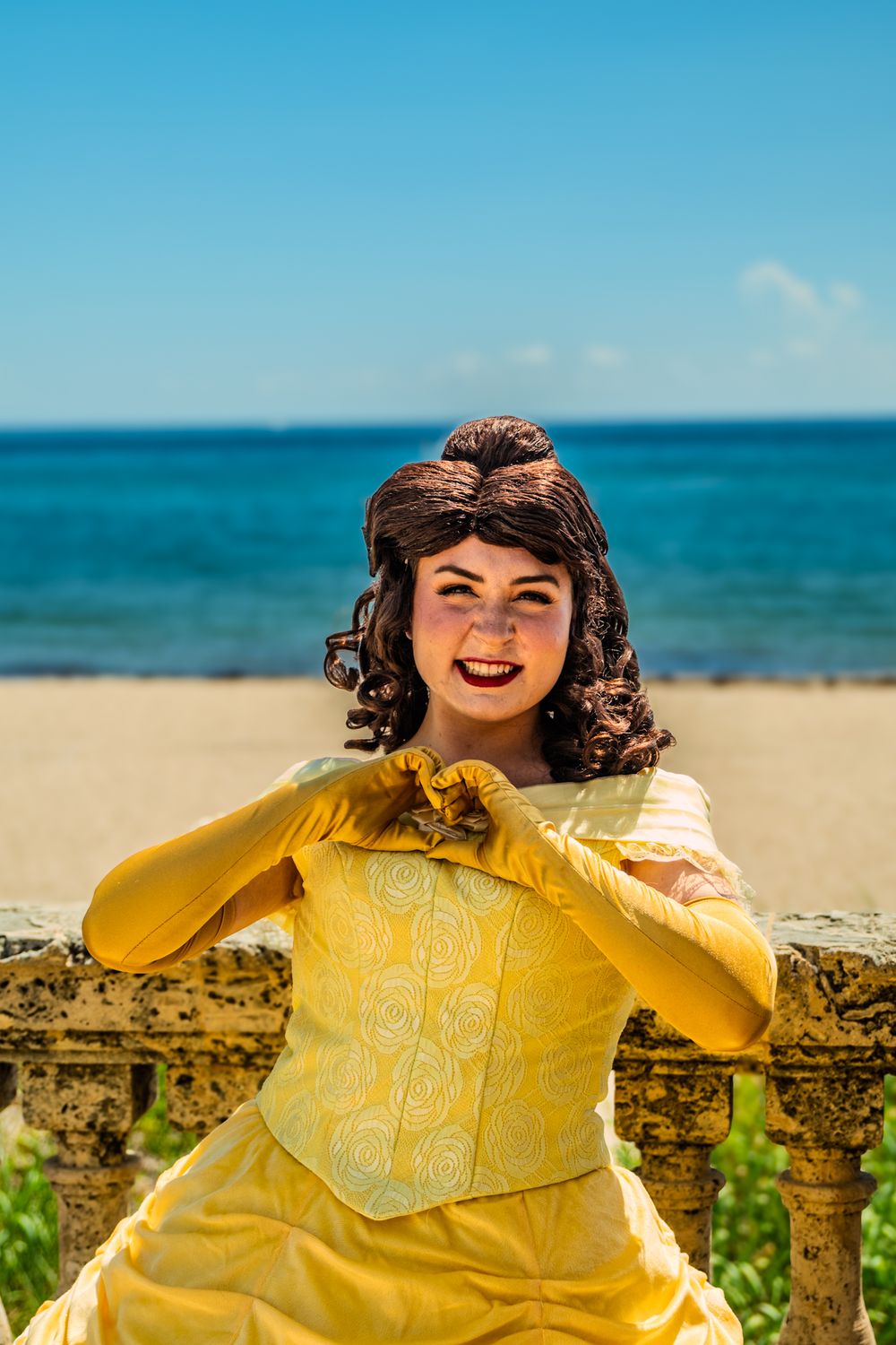 Person in yellow dress posing against ocean backdrop on sunny beach.