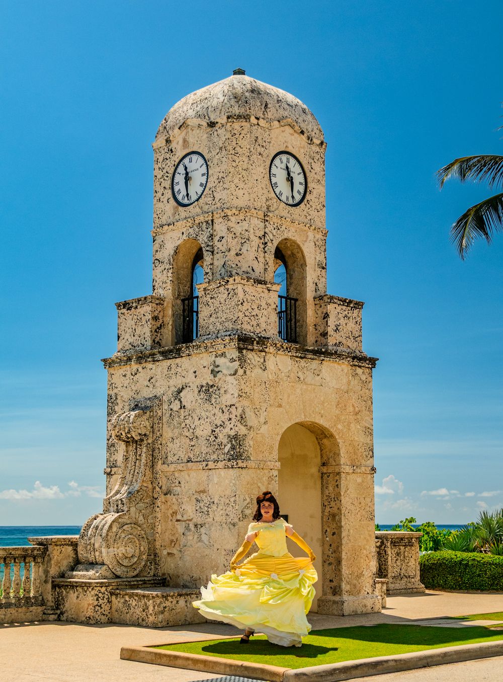 Historic stone watchtower with clock faces against bright blue sky at Palm Beach Worth Avenue.
