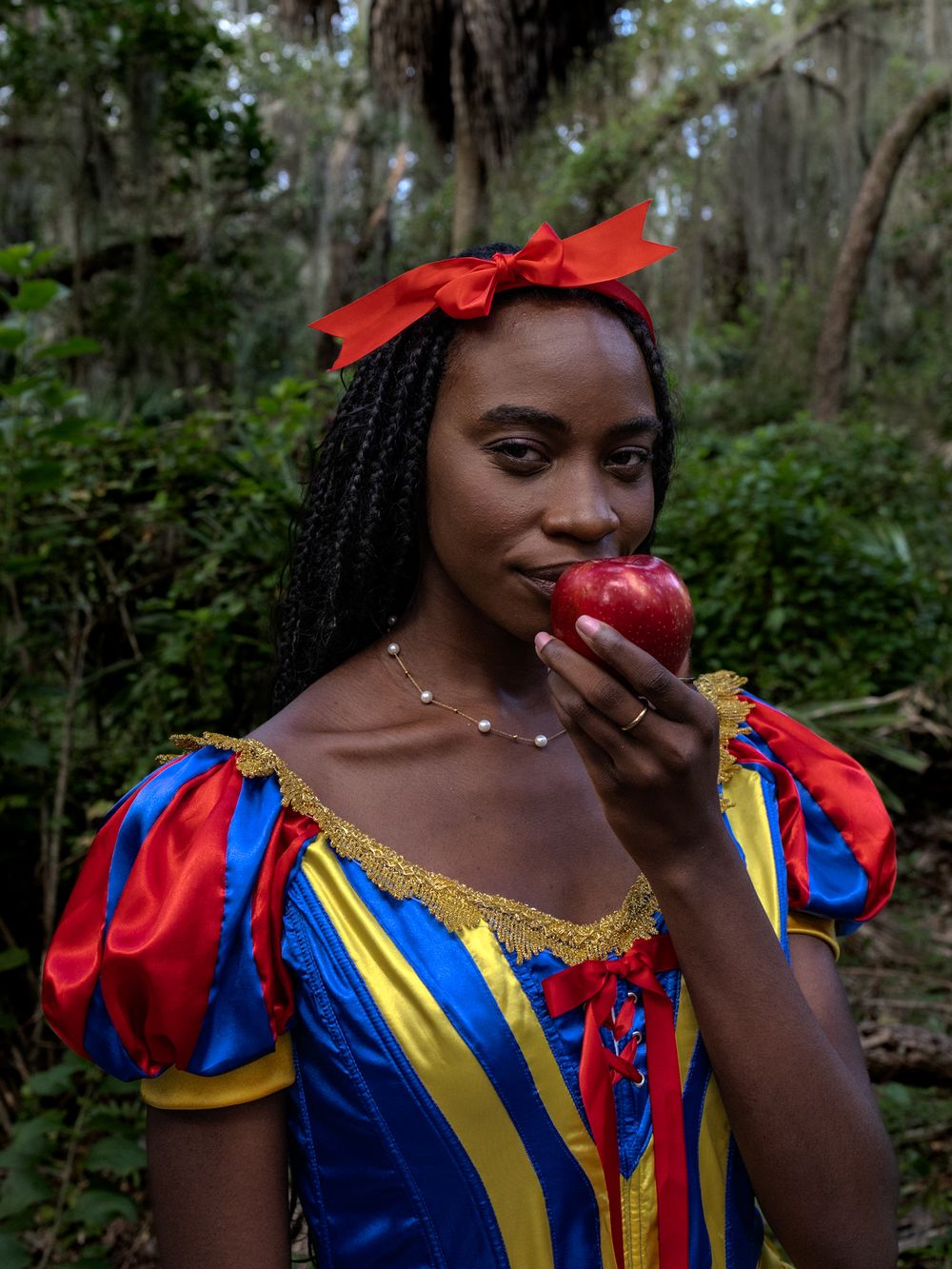 A colorful Snow White inspired costume is worn in a forest setting with palm trees.