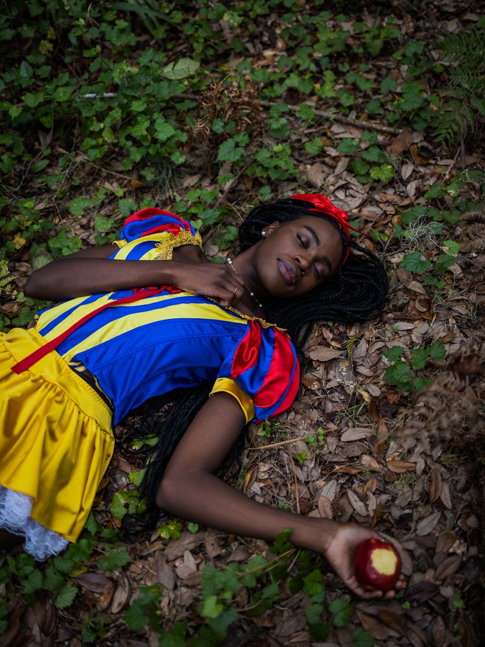 A yellow and blue costume lies among fallen leaves in a forest setting.