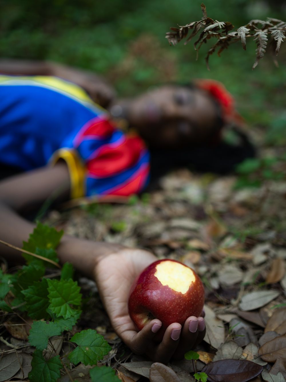 A bright red apple is held against a background of fallen leaves.
