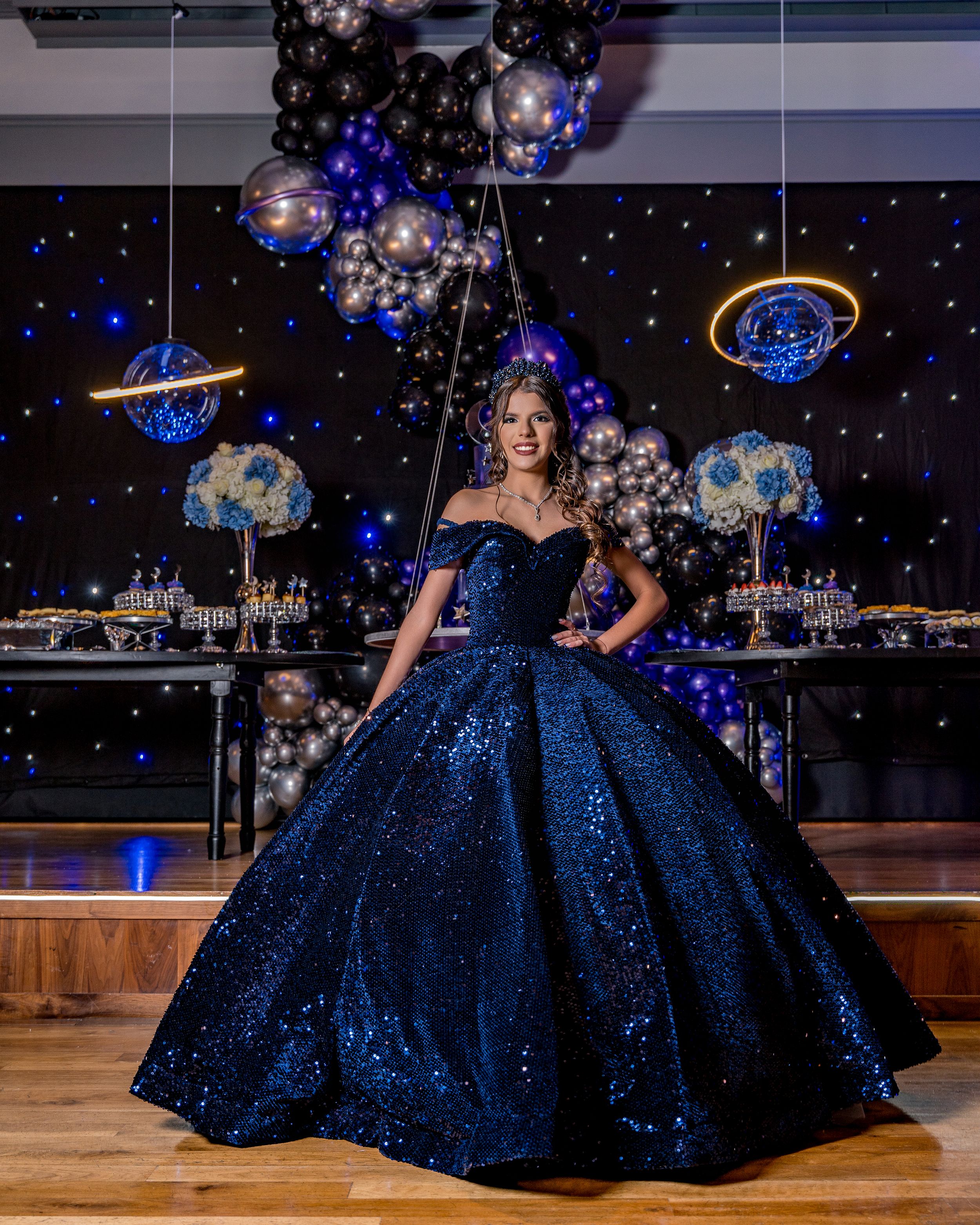 A sparkling navy blue ball gown with off-shoulder design reflects light against a dark backdrop at a formal event venue.