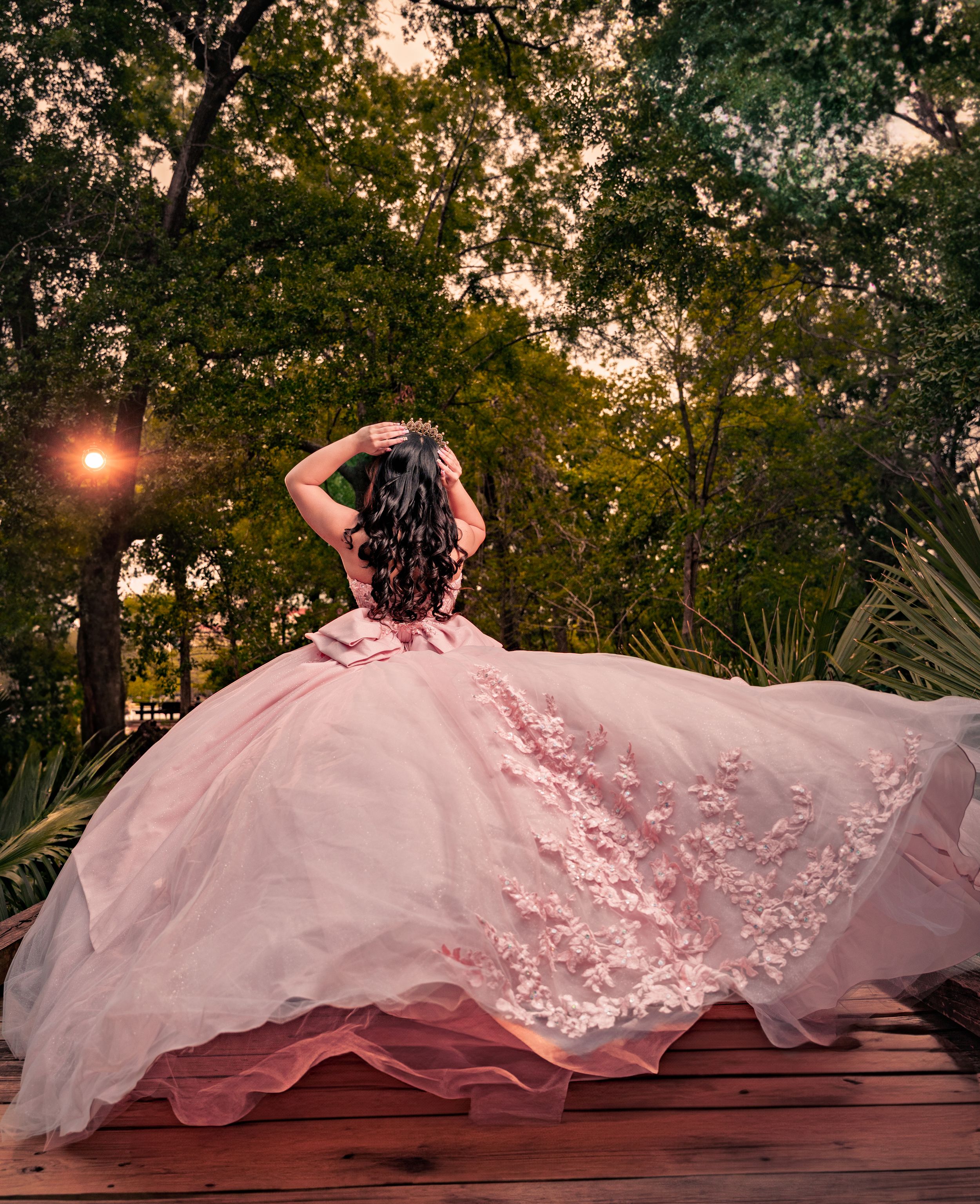 A flowing wedding gown train cascades dramatically across a wooden deck at sunset with elegant lace details.