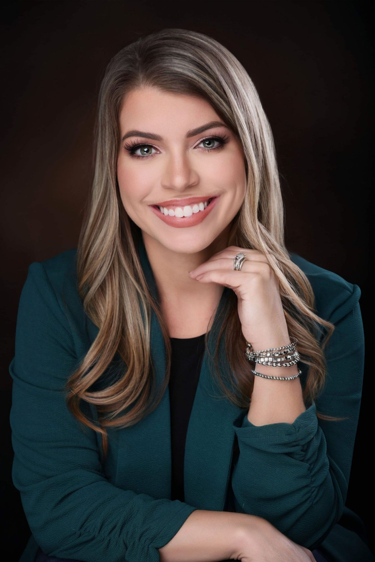 Professional portrait showing blonde hair and emerald green blazer against dark background with warm smile.