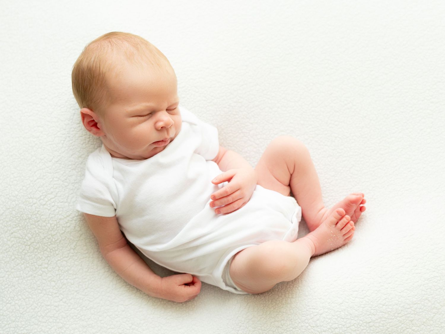 Four separate photos show a sleeping baby dressed in white against a light background in different peaceful poses.