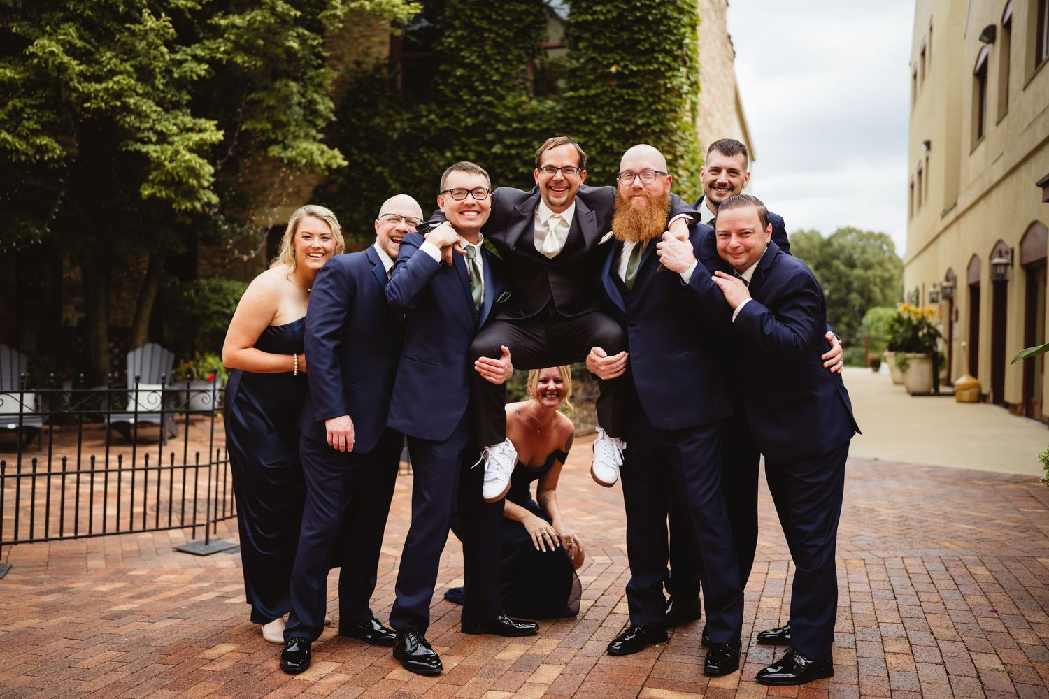 A group wearing navy suits poses together on brick walkways outside a building in multiple candid shots.