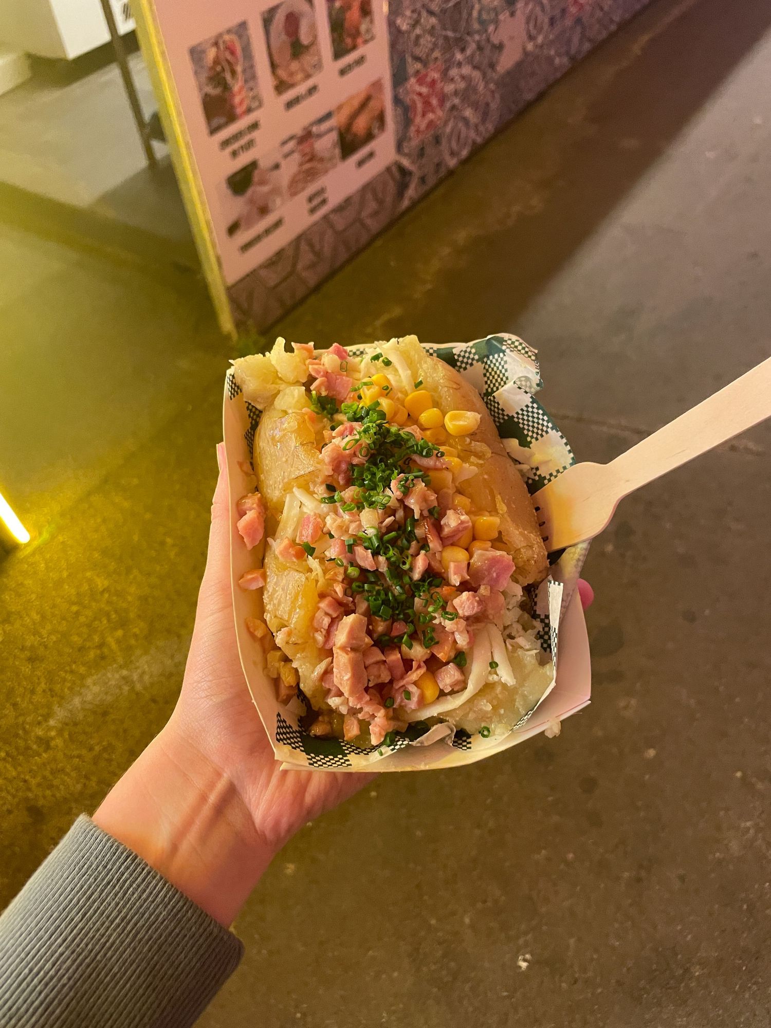 A hand holds a paper boat filled with spicy tuna poke garnished with fresh herbs and green onions.