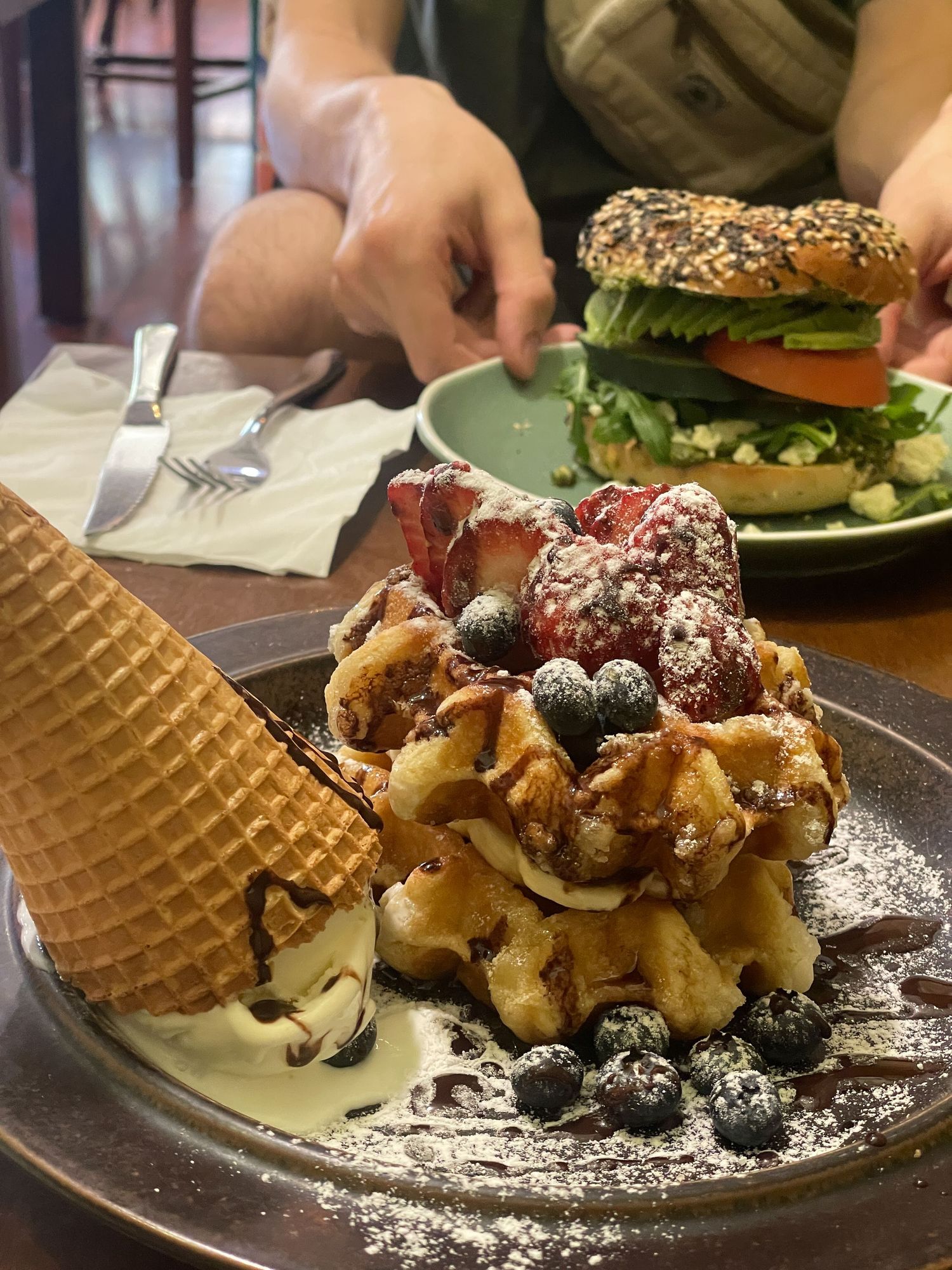 A close-up shot of dessert plates featuring waffles, berries, and powdered sugar served on dark plates.