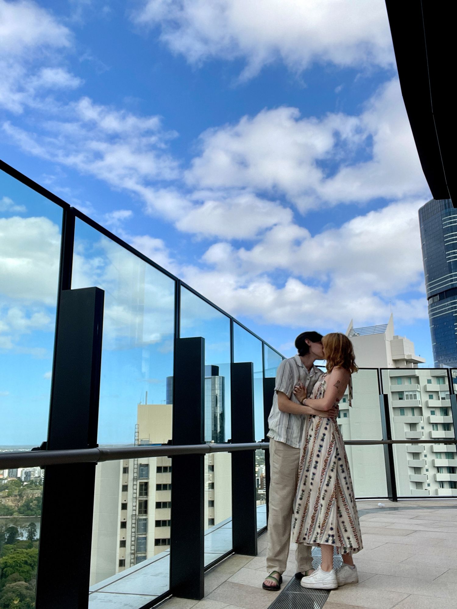 Someone wearing a floral dress standing on a rooftop terrace with city buildings and blue sky in background.