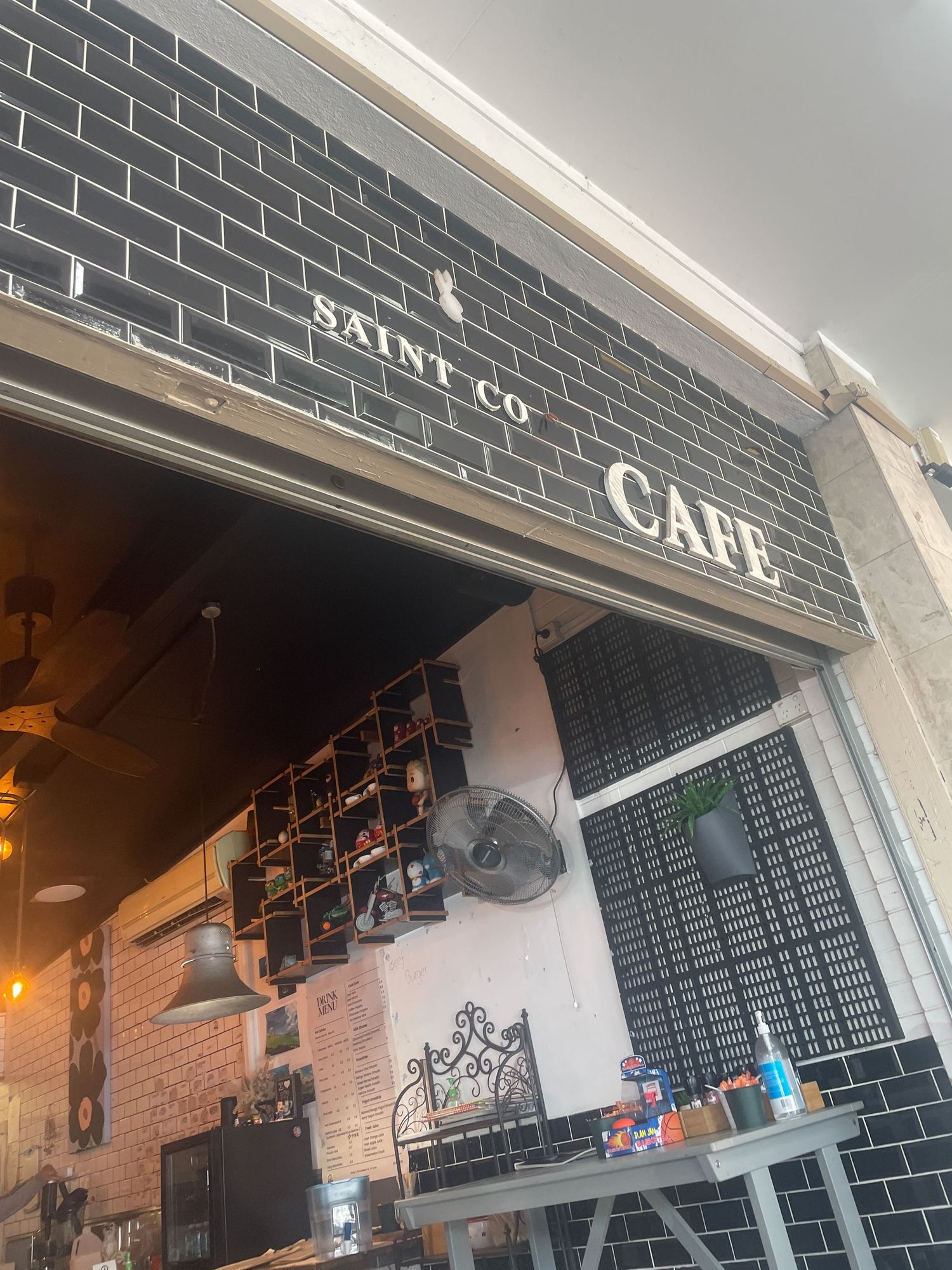 Black tiled storefront with 'Saint Co Cafe' signage and exposed brick interior visible through entrance.