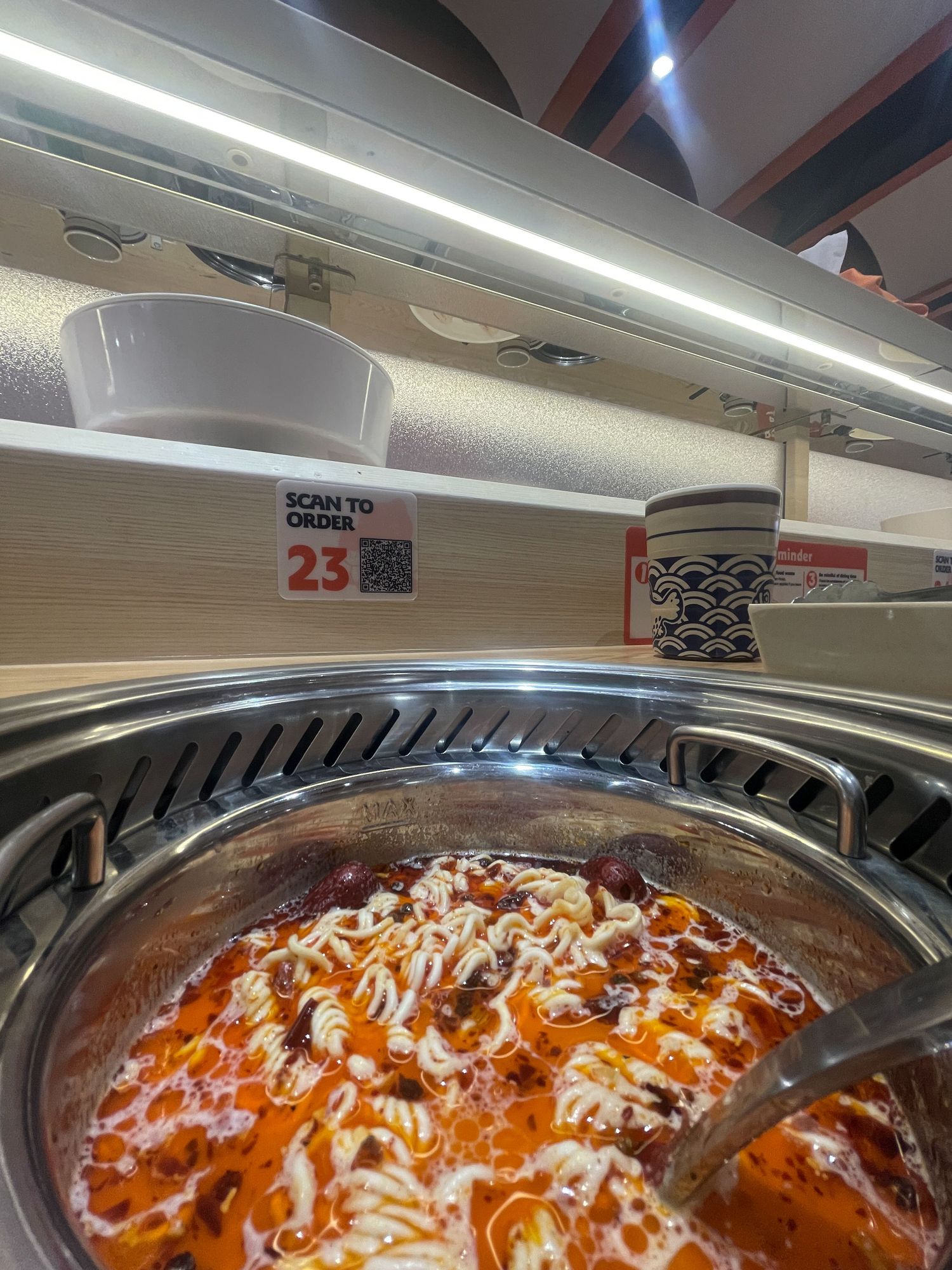 A close-up view of baked pasta with melted cheese and red sauce in a serving tray under bright fluorescent lighting.
