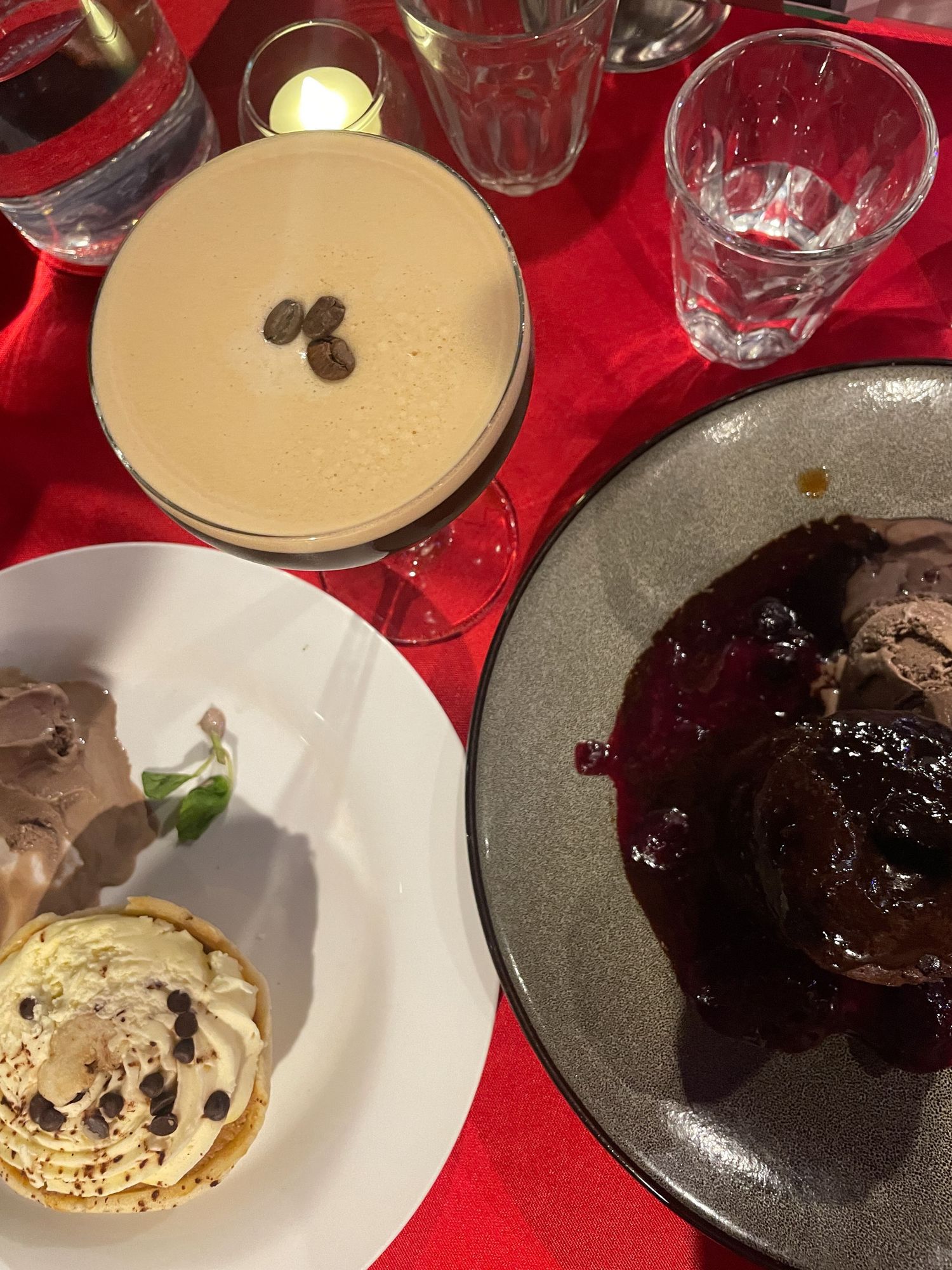 Plated desserts including chocolate cakes and cream garnishes served on white and dark plates on a red tablecloth.