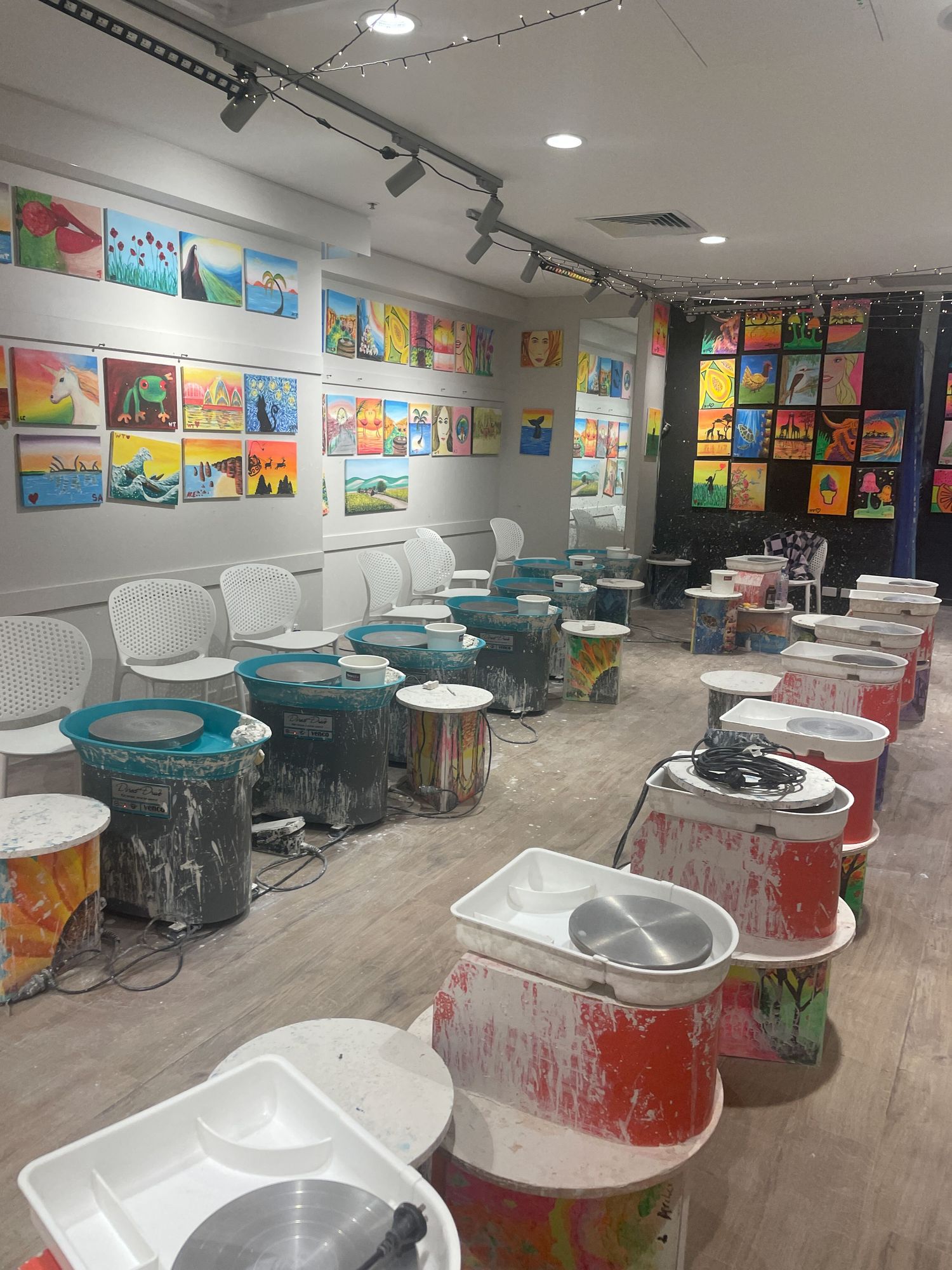 Empty art classroom with white barber-style chairs and colorful children's artwork displayed on walls.
