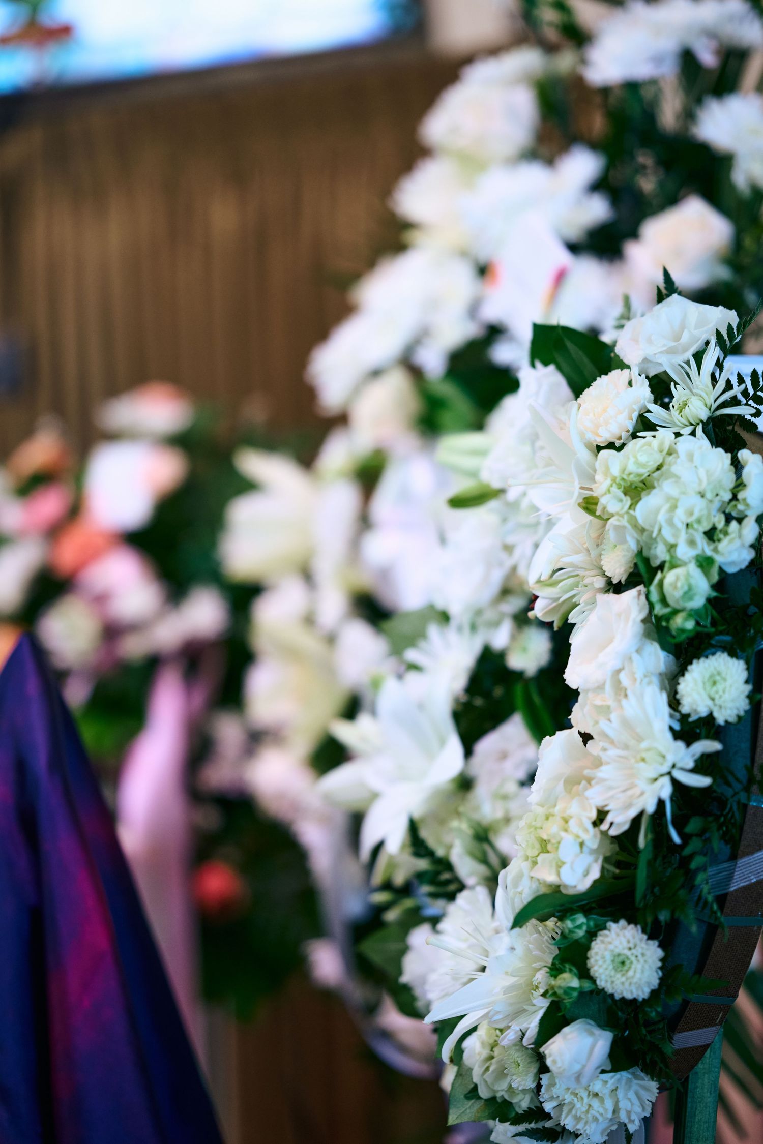 White carnations and roses decorate a pew end at a formal event with soft blurred background and purple accents.