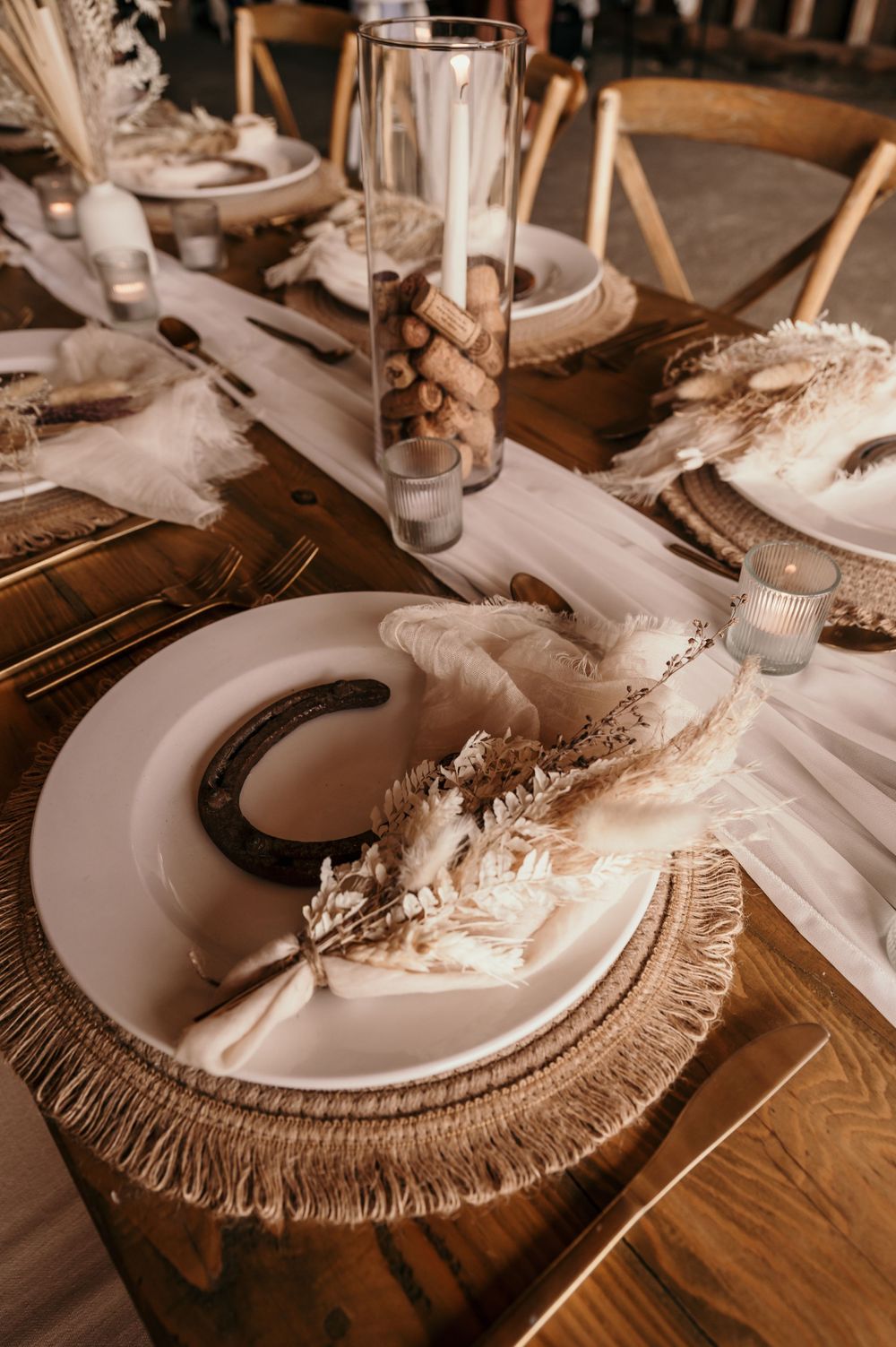 Elegant table setting with dried pampas grass decoration on white plates and fringe chargers in warm neutral tones.