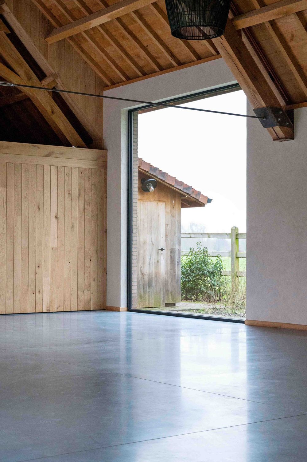 Converted barn interior with wooden ceiling and large windows overlooking countryside.