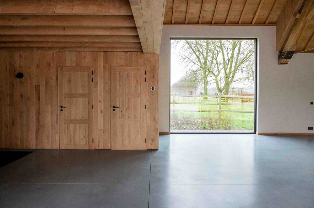 Rustic wooden ceiling beams frame a bright attic space with large windows.