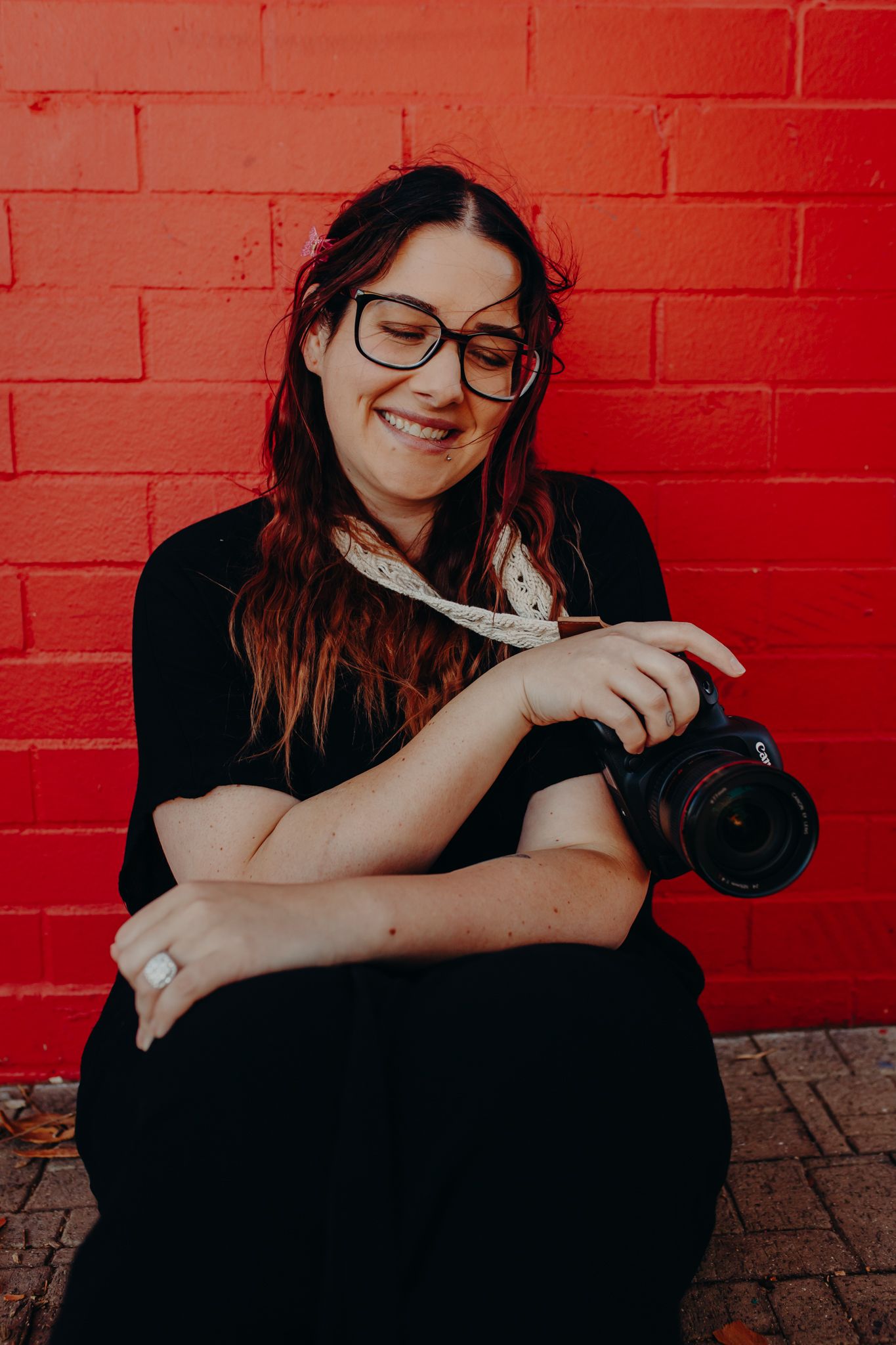 Portrait of photographer with camera against vibrant red brick wall background.