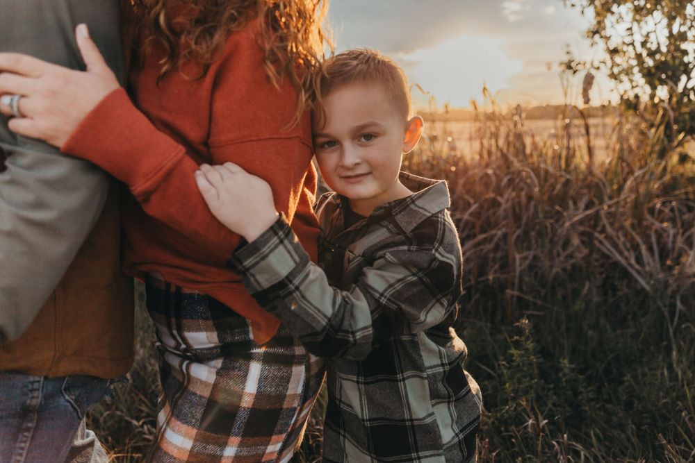 Young child in plaid shirt smiling and embracing in golden sunlit field. terre haute family wedding photographer parke county