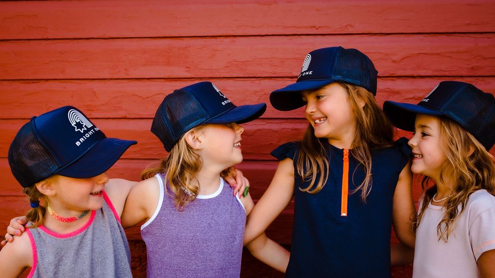 Four children laugh together while wearing branded hats