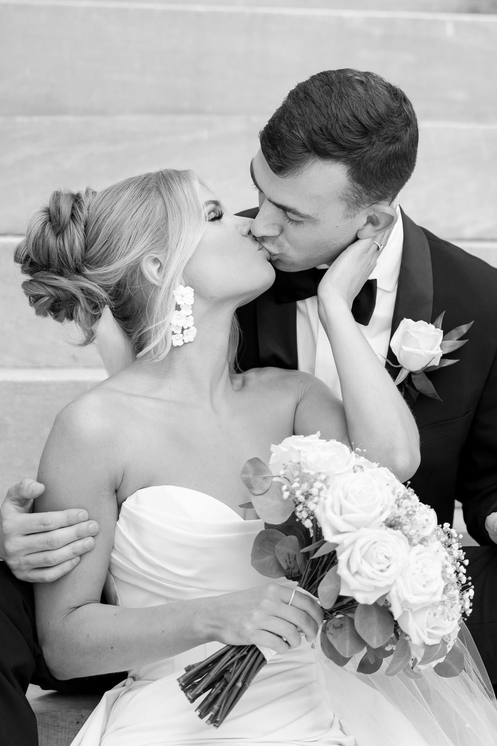 Black and white romantic wedding photo of newlyweds sharing a kiss while seated on the steps the Merchant Exchange building in Philadelphia