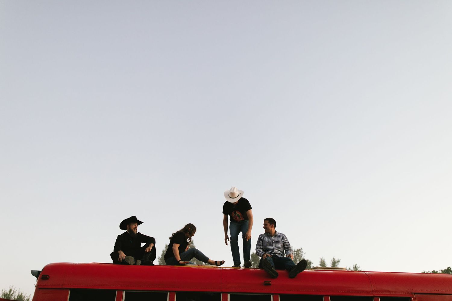Silhouettes of people sitting on top of red vehicle against light sky.