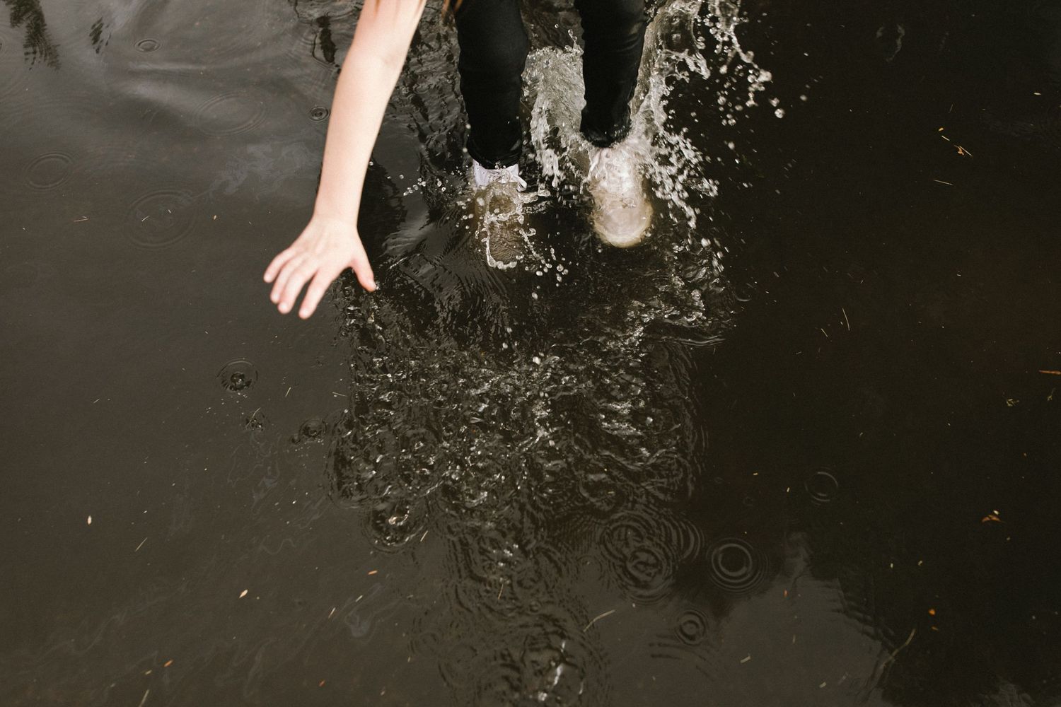 Feet splashing in dark water creating ripples and spray.