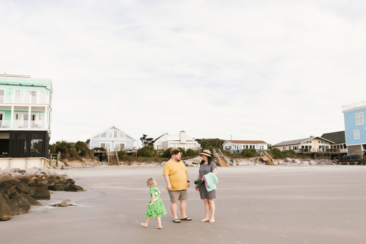 Family enjoying time together on a beach with pastel-colored beach houses in the background.