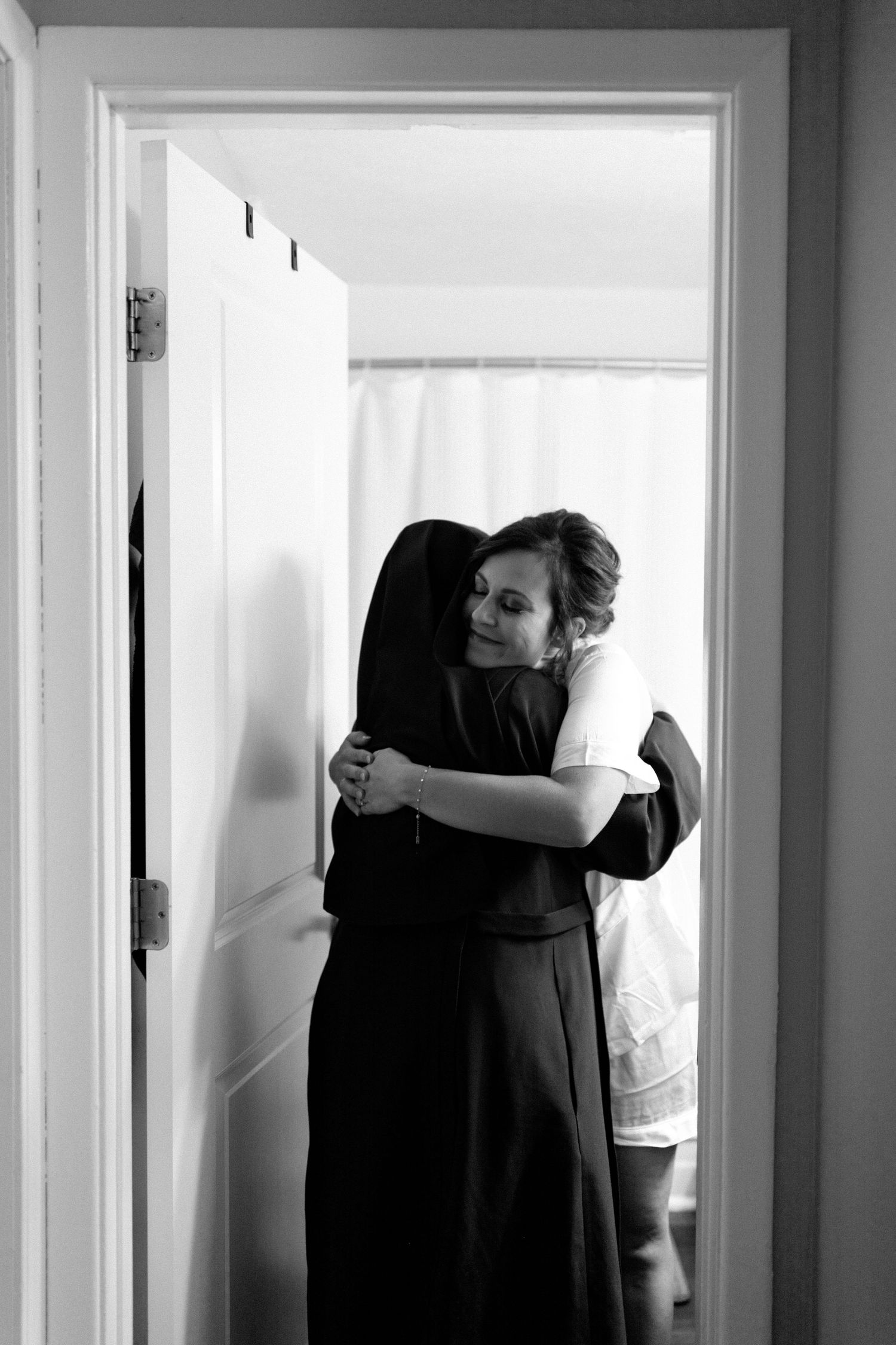 A black and white photograph captures an emotional embrace in a doorway.