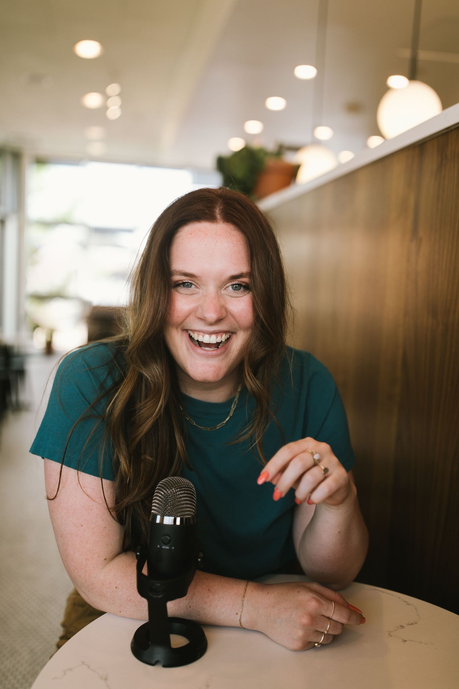 A person sits at a table with a microphone, expressing joy during what appears to be a podcast recording.