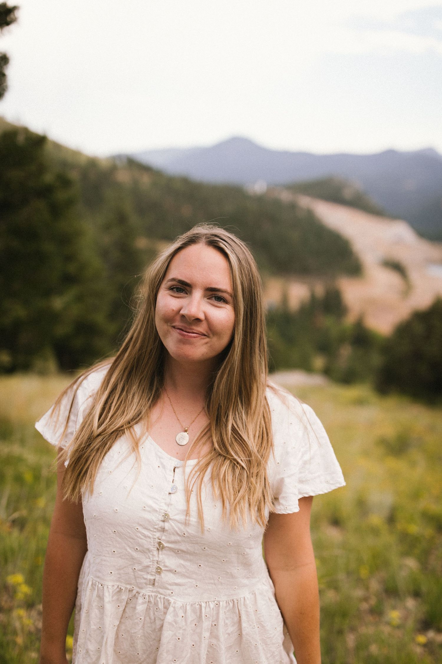 A person stands in a white dress against a scenic mountain backdrop.