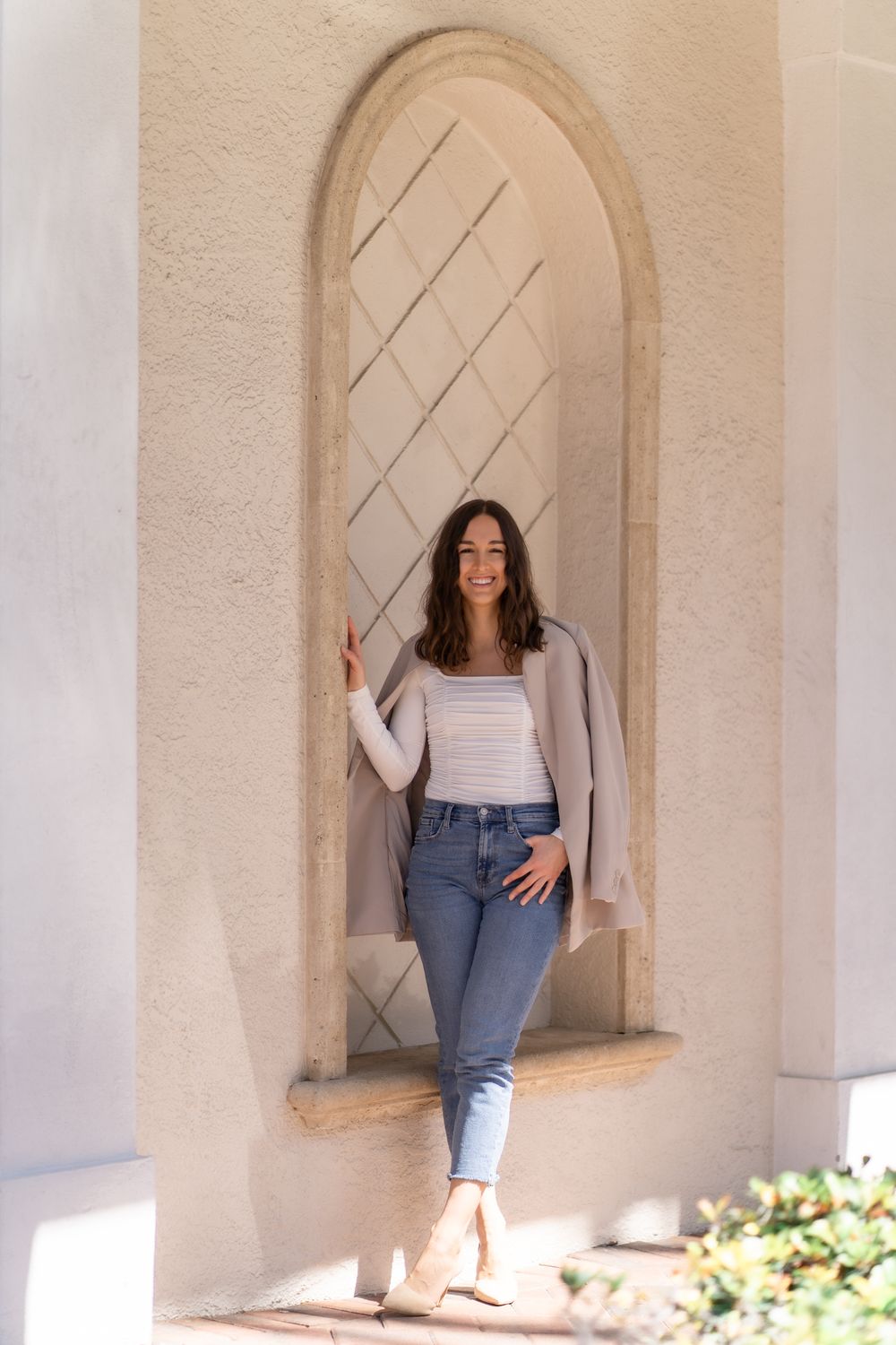 Casual fashion portrait in archway with striped crop top, cardigan, jeans and beige boots against textured wall.