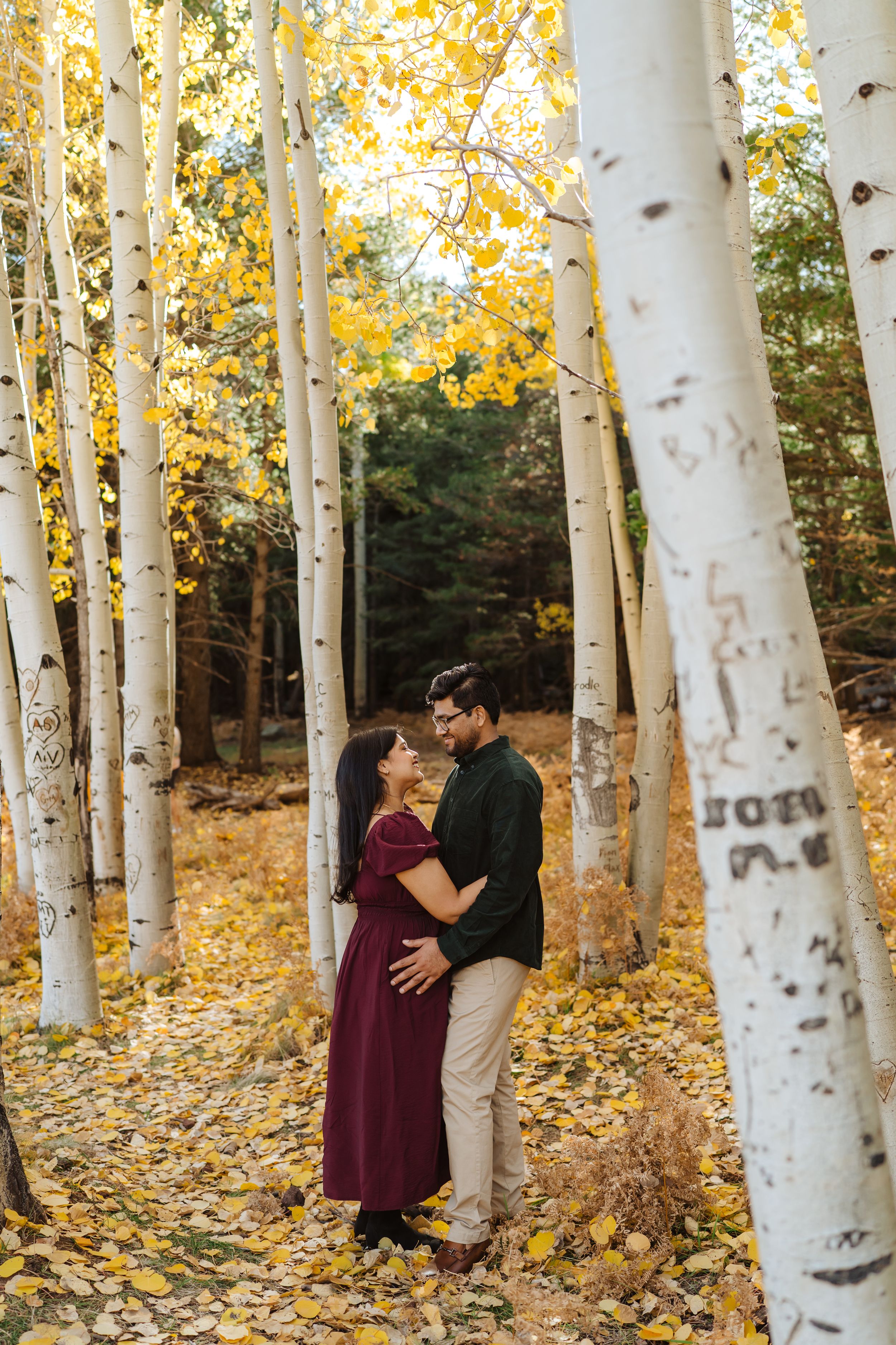 A couple embraces among white birch trees with golden autumn leaves scattered on the aspen forest floor in Flagstaff, Arizona.