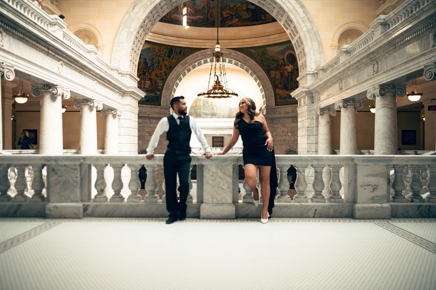 Couple holding hands in elegant marble rotunda with ornate columns and painted ceiling dome.