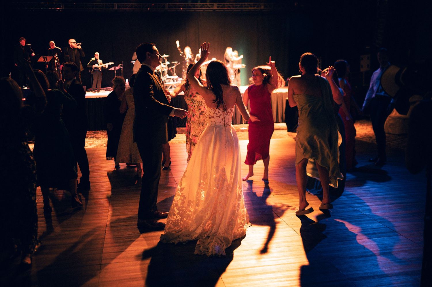 Bride and guests dancing under warm lights at a romantic wedding reception on a wooden dance floor.