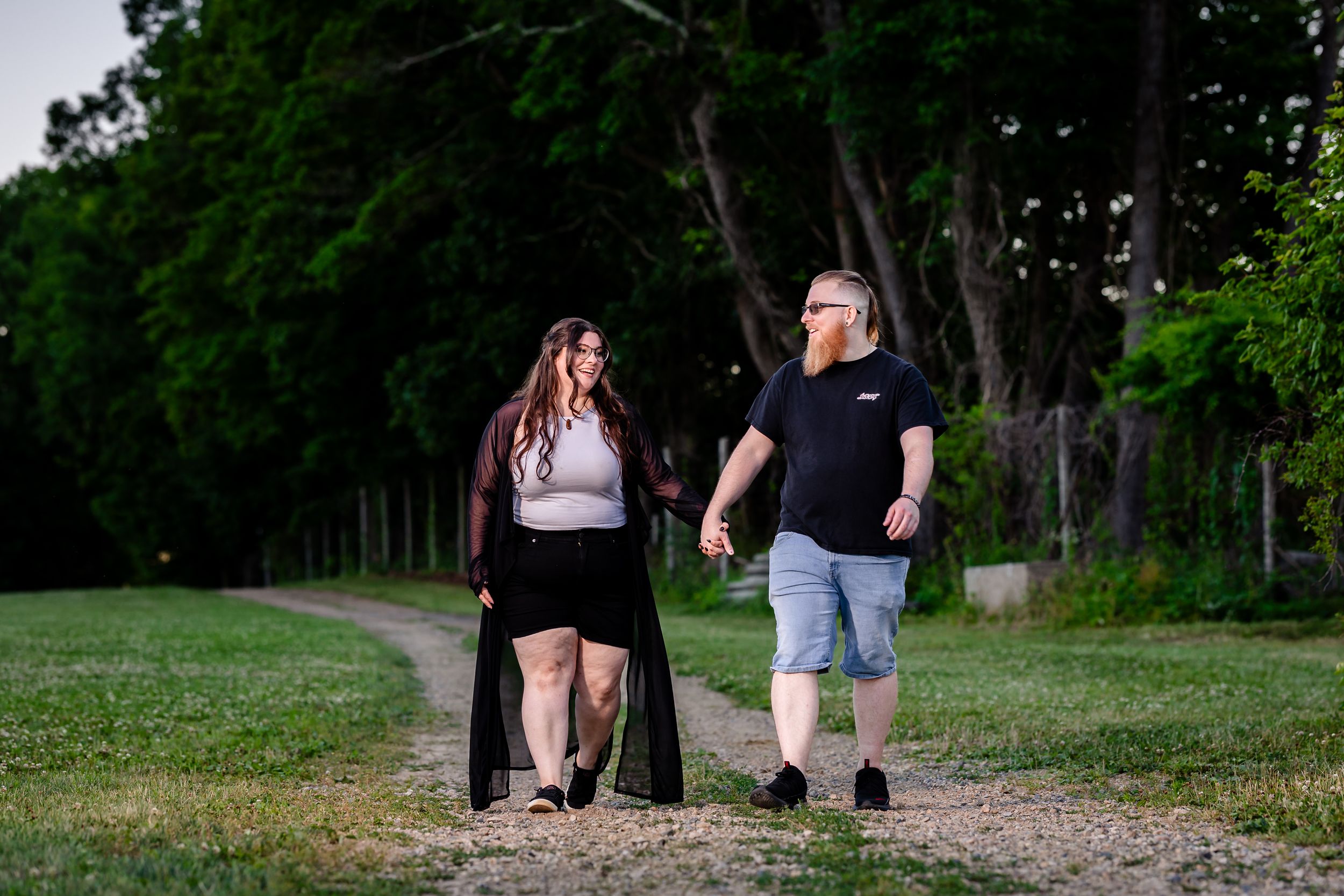 Couple walking together on a gravel path through an open green park at sunset.