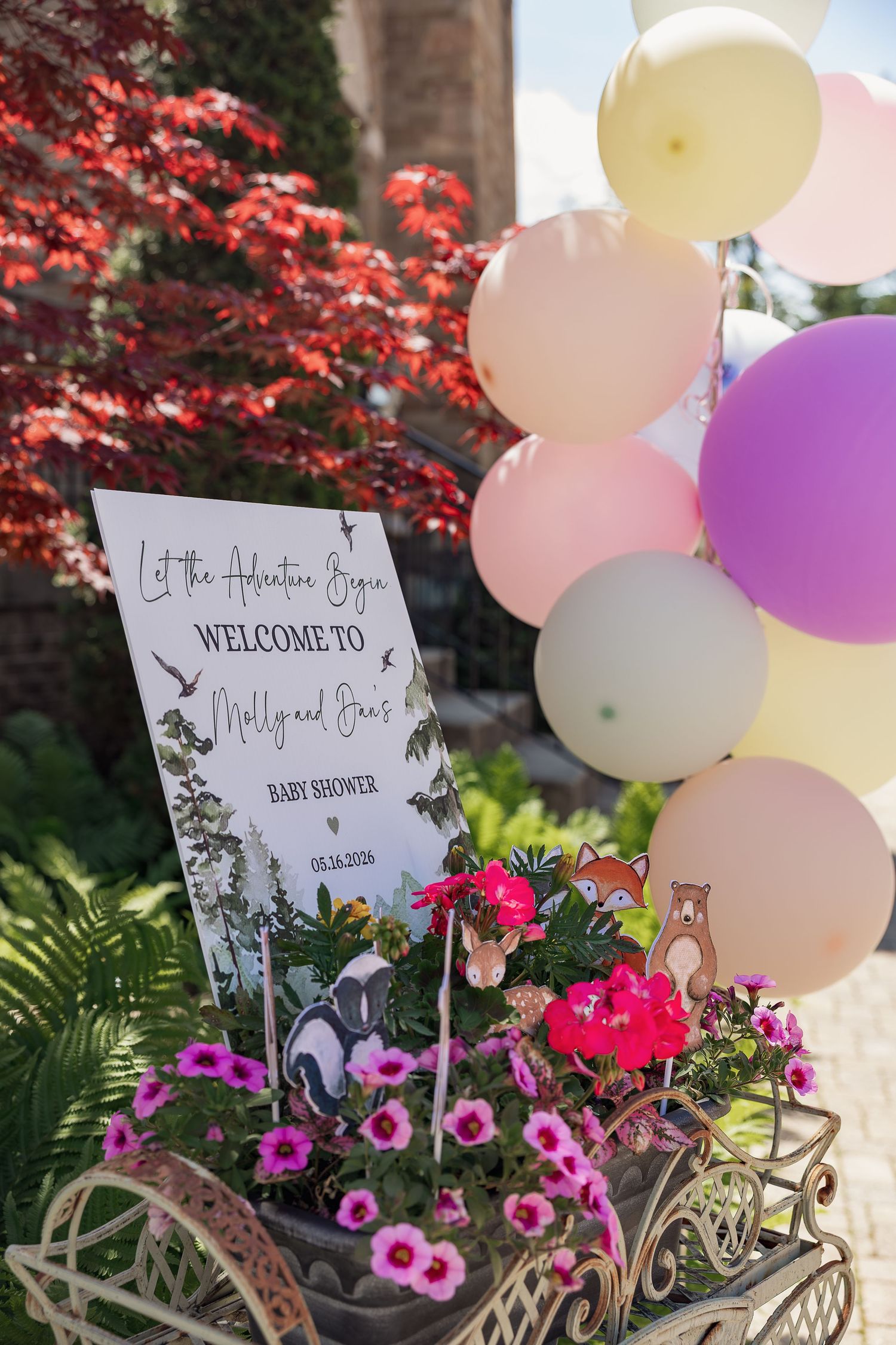 Baby shower welcome sign for Molly and Evan surrounded by pink flowers and pastel balloons in a garden setting.