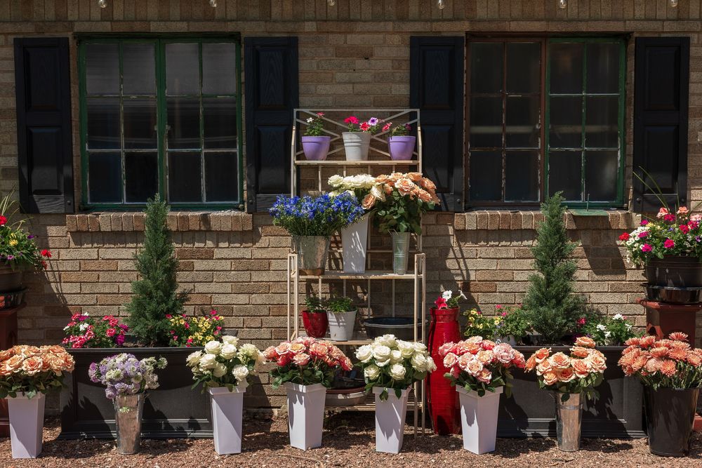 Colorful flower shop display with roses and mixed blooms in white buckets arranged outside a rustic brick building.
