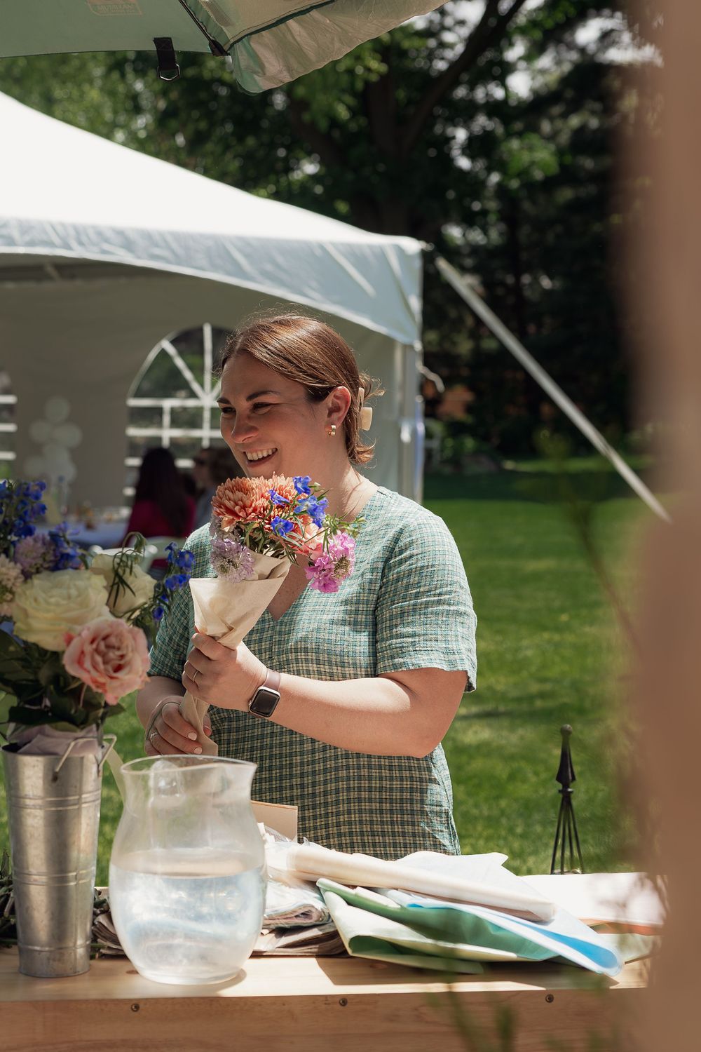 Smiling woman holding a colorful flower bouquet at an outdoor market stall on a sunny day.