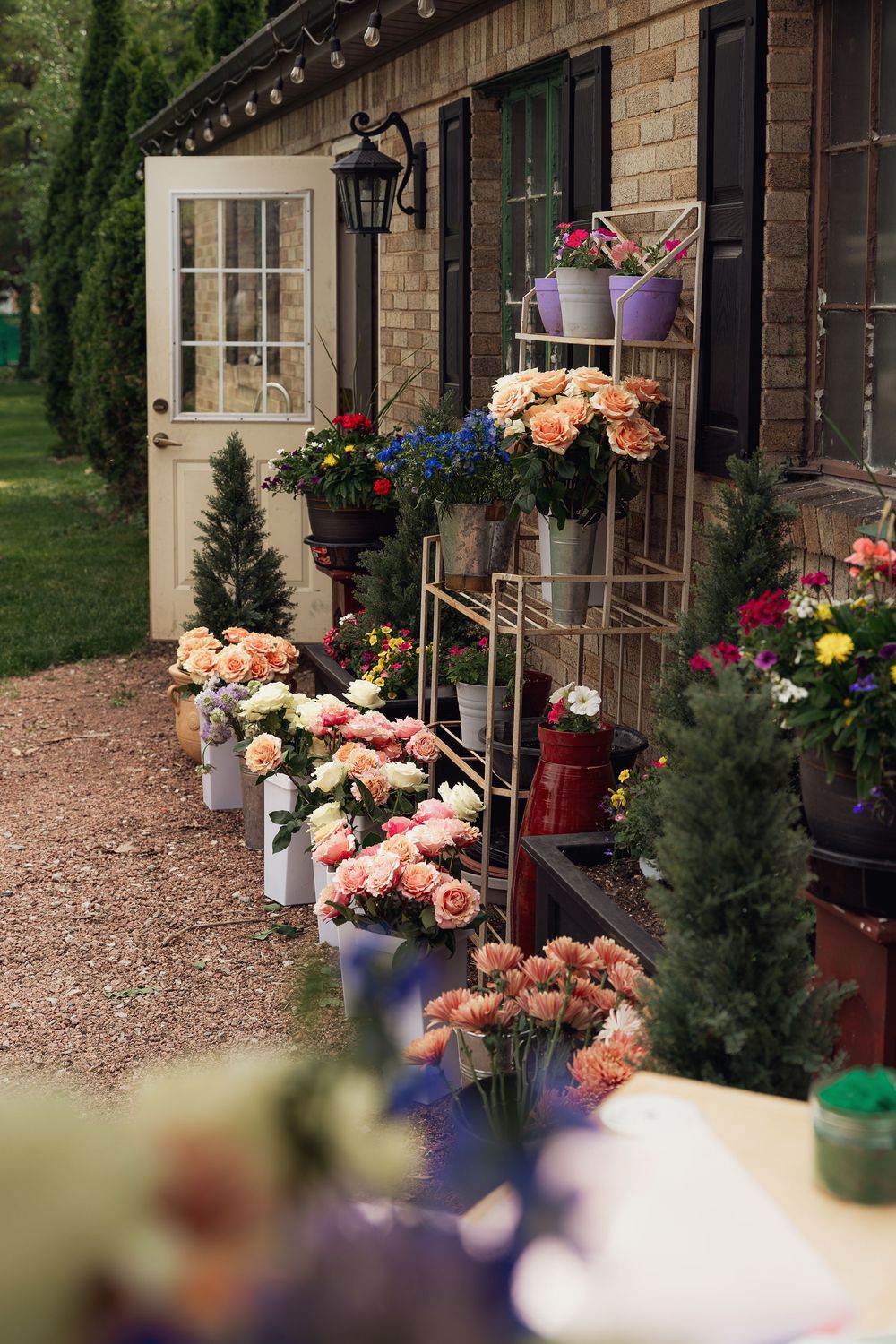 Colorful flower arrangements displayed outside a brick building with a metal rack holding blooms in buckets near a white door.