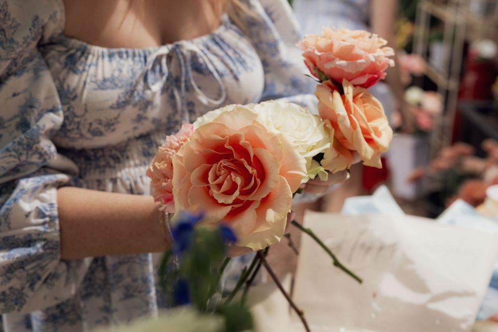 Woman in floral dress arranging peach roses, creating a beautiful floral bouquet arrangement.