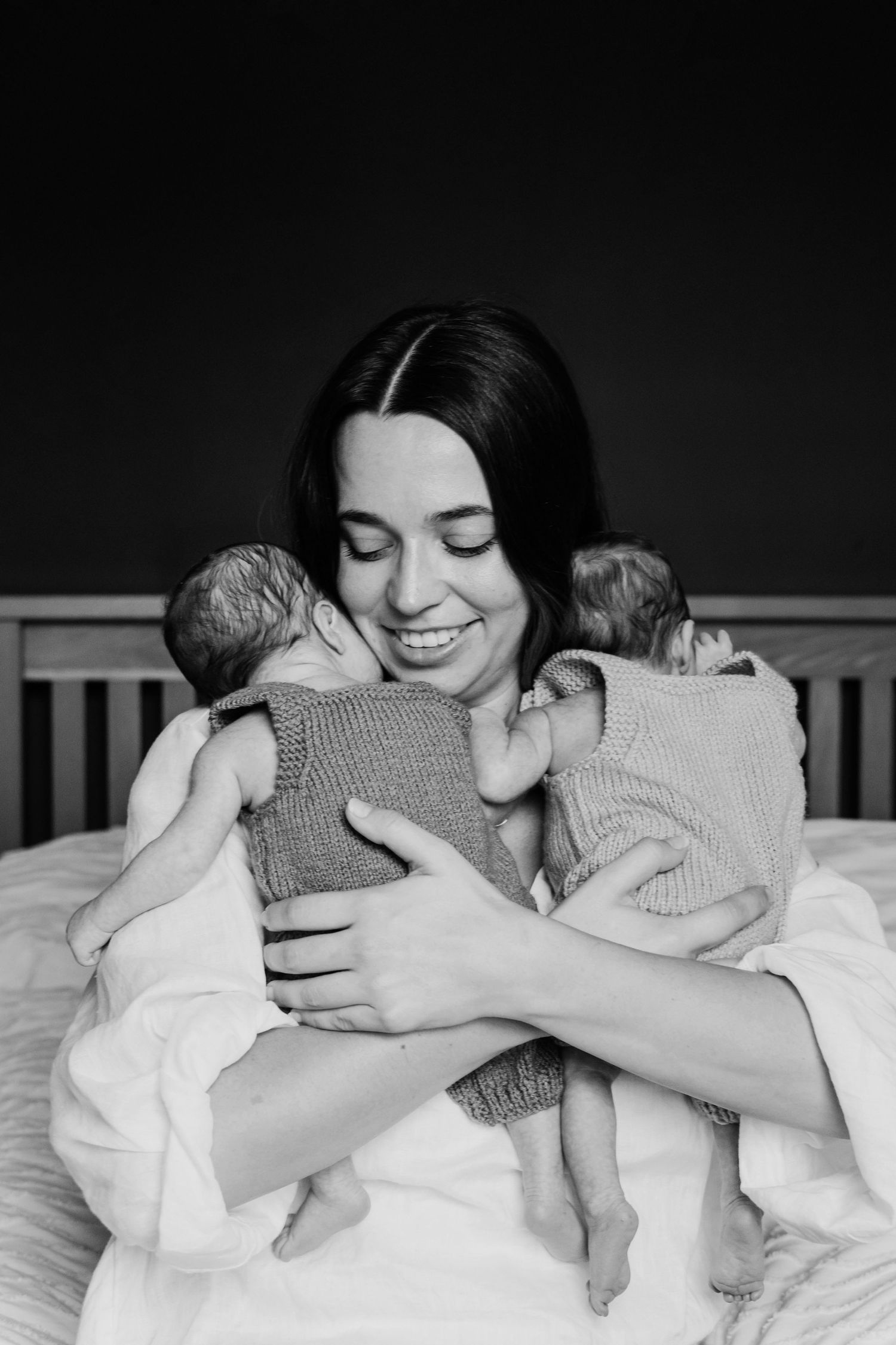 Black and white portrait of a mother cuddling her newborn twins during an in-home lifestyle session.