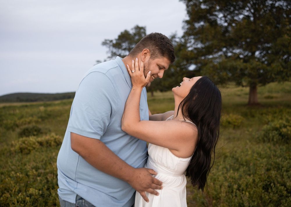 Couple sharing a romantic moment outdoors in a green field, man in blue shirt and woman in white dress.