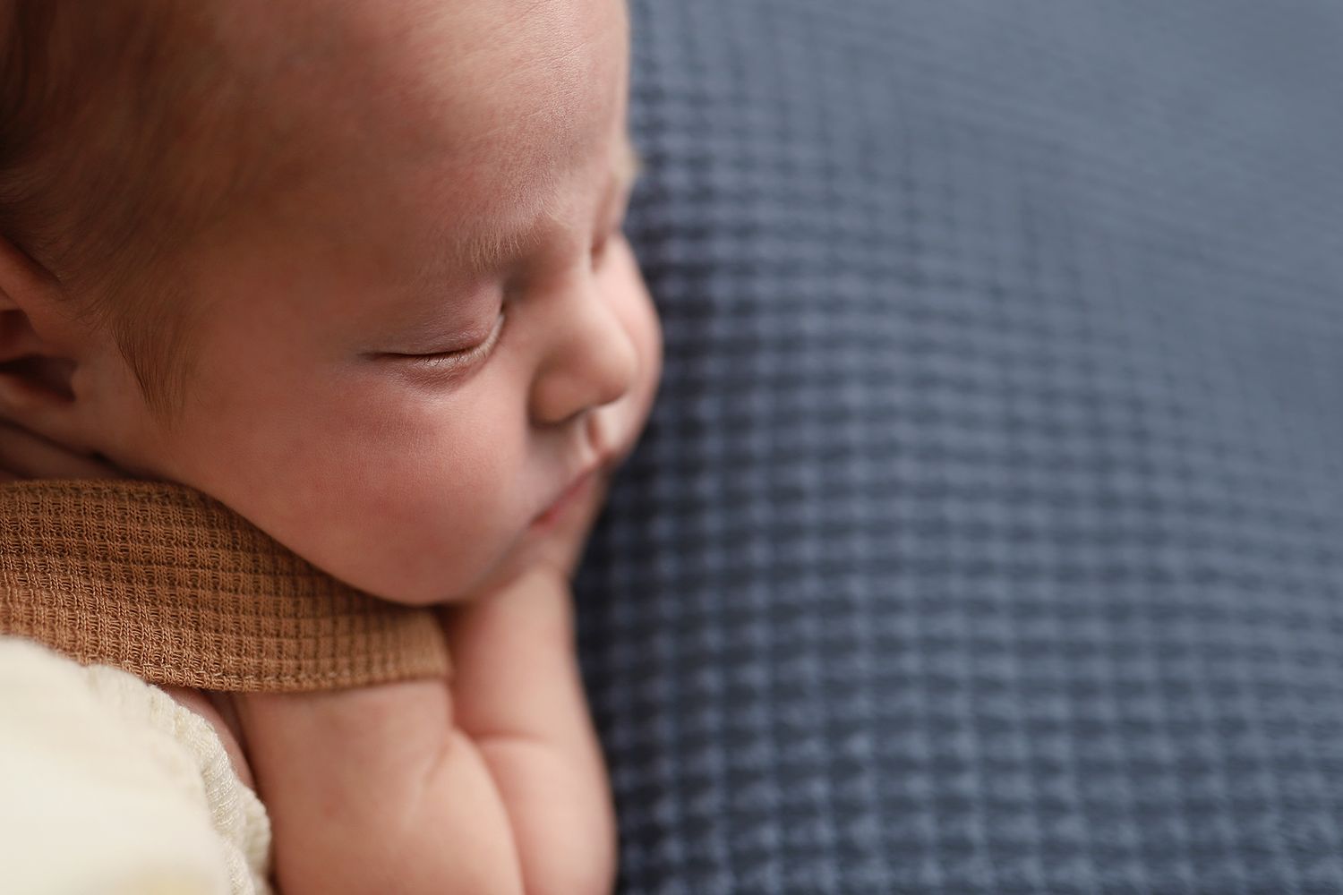 Peaceful newborn baby sleeping on a soft blue textured blanket, close-up portrait photography. Newborn photography studio in Orem