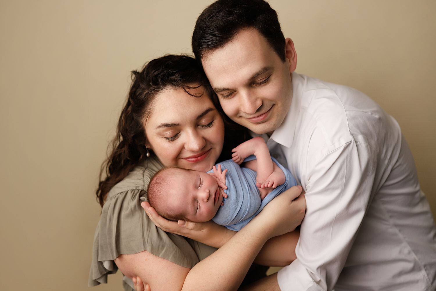 A couple tenderly holds their sleeping newborn baby wrapped in blue during a professional studio portrait session.