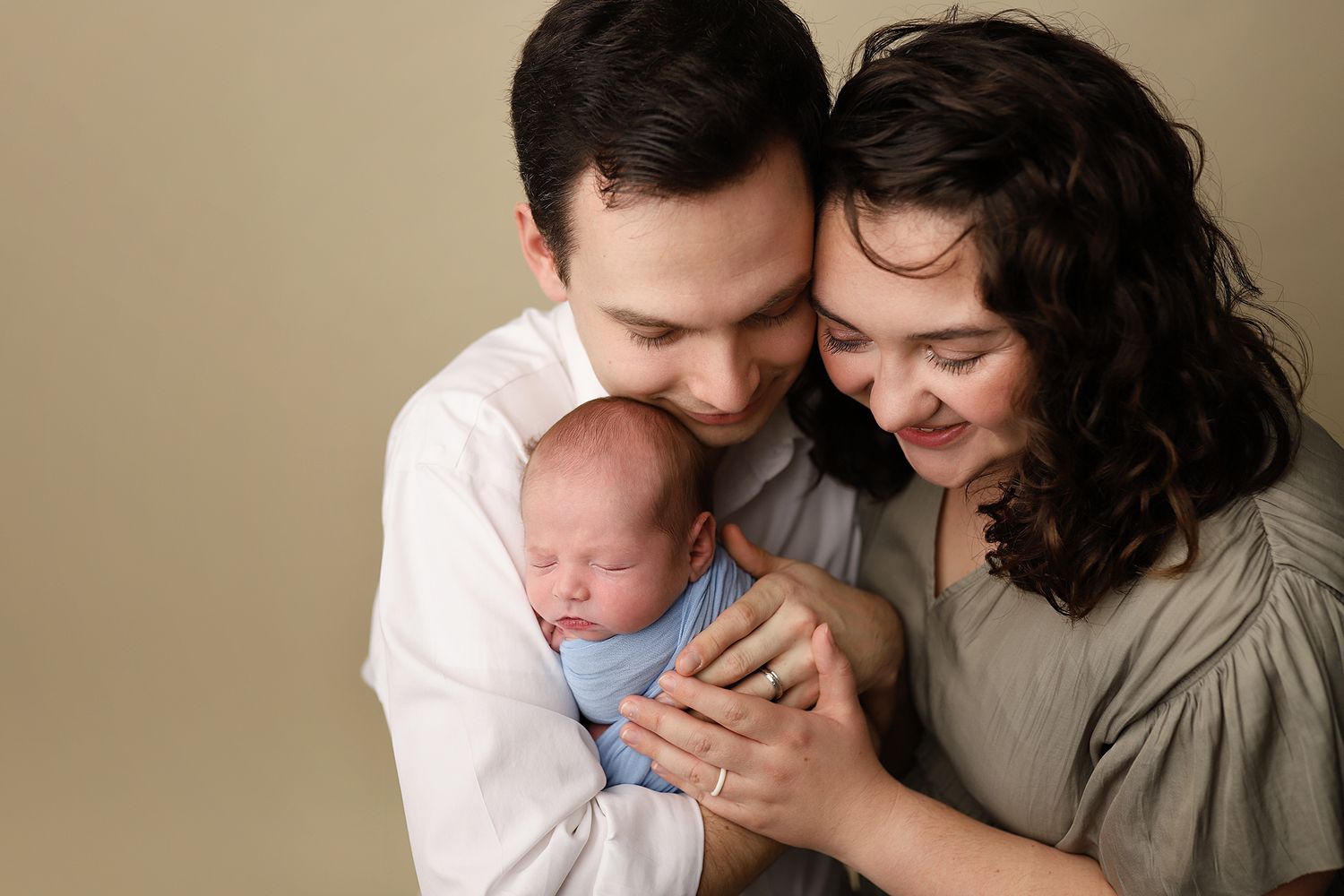 New parents tenderly cradle their sleeping newborn wrapped in blue during a professional studio portrait session. newborn family portraits