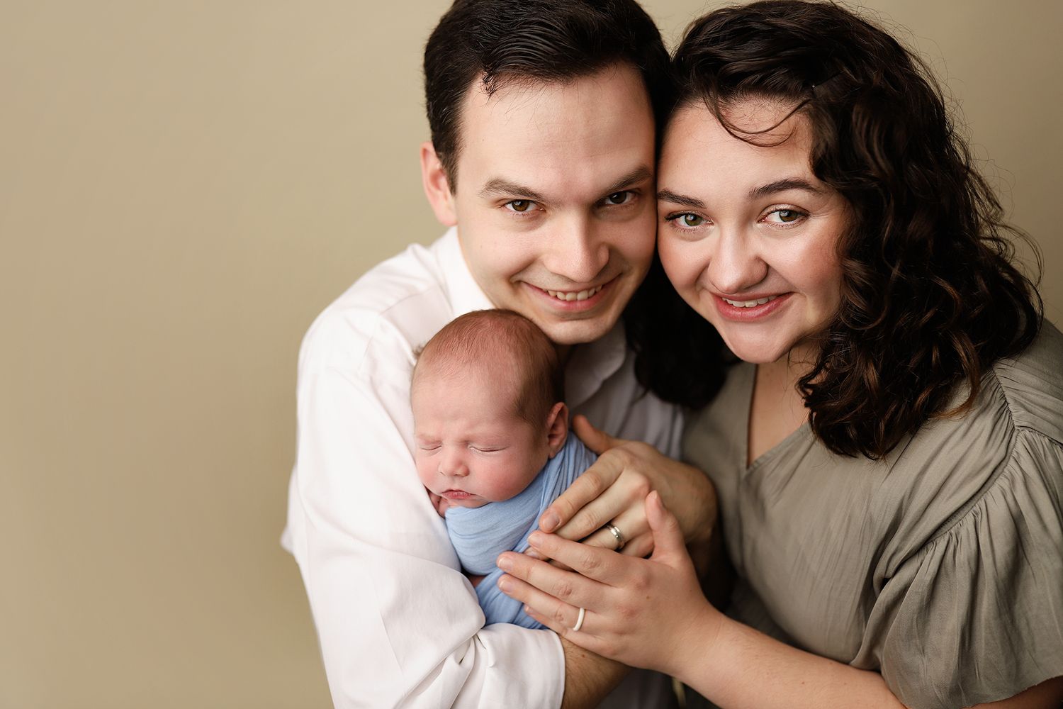 Happy parents smiling and holding their sleeping newborn baby wrapped in a blue swaddle.